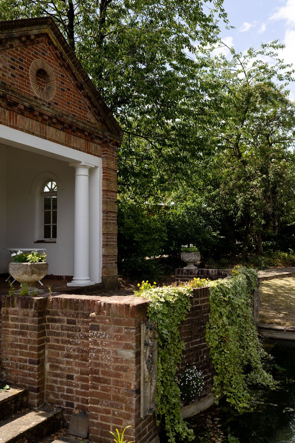 Red brick building exterior with white columns and lush green foliage surrounding the entrance.