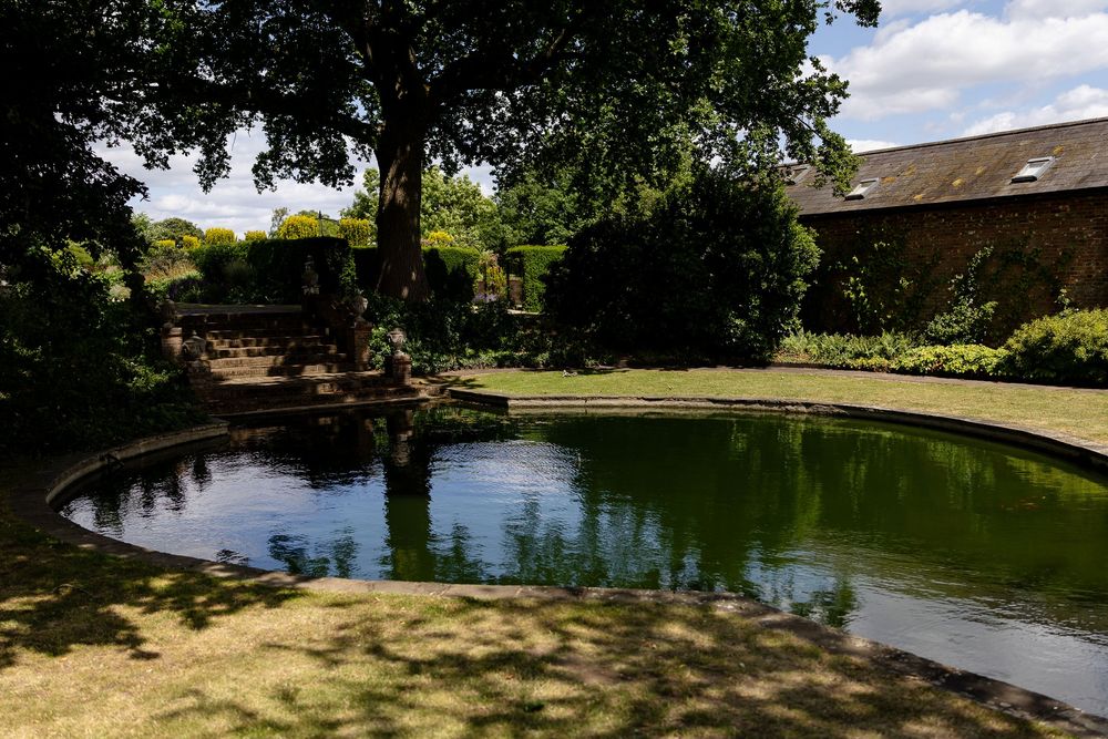 A tranquil curved pond surrounded by trees and greenery in a peaceful garden setting on a sunny day.