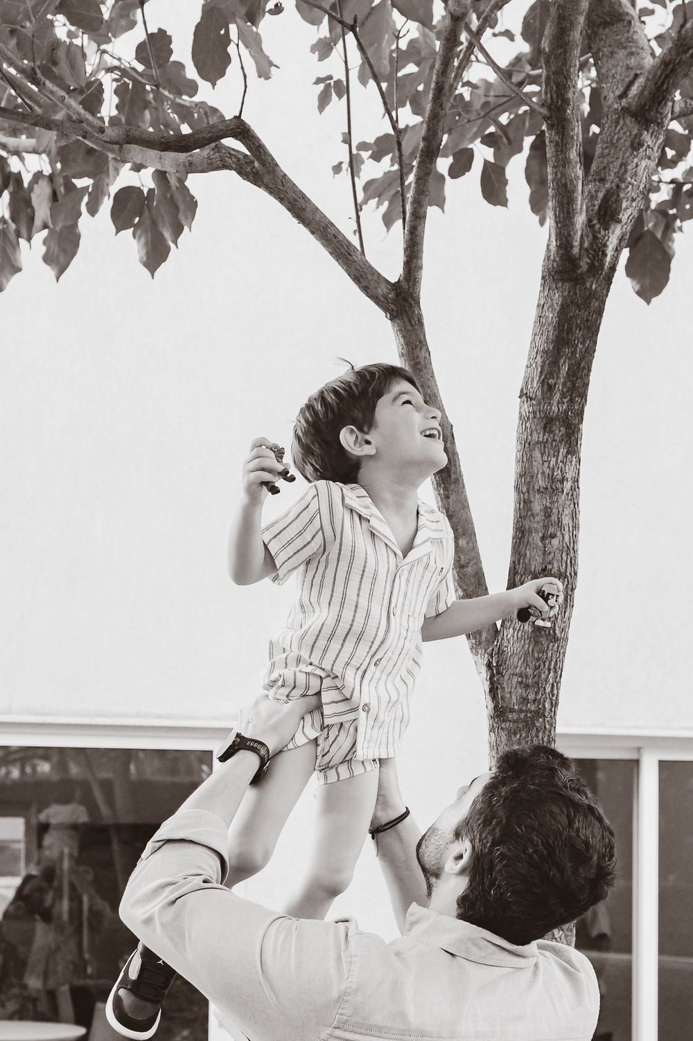 Two brothers laugh and play together outdoors under a tree in black and white vintage-style photography.