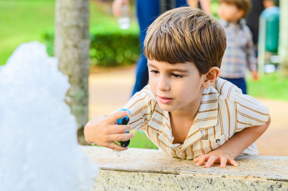 Child in striped shirt leans over concrete surface while observing something with curiosity in outdoor setting.