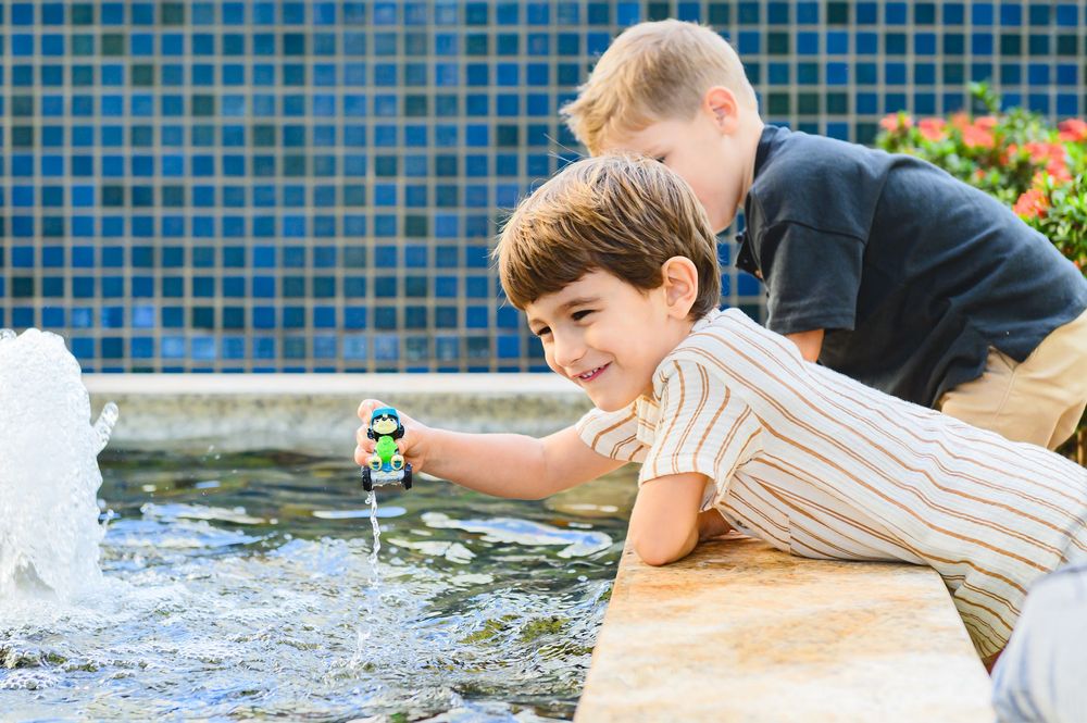 Children play with toy at edge of fountain pool with blue mosaic tile wall in background.