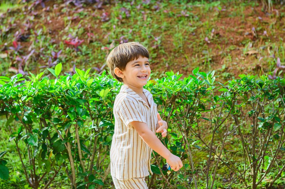 A young child in striped clothing plays and laughs joyfully in a lush green garden setting.