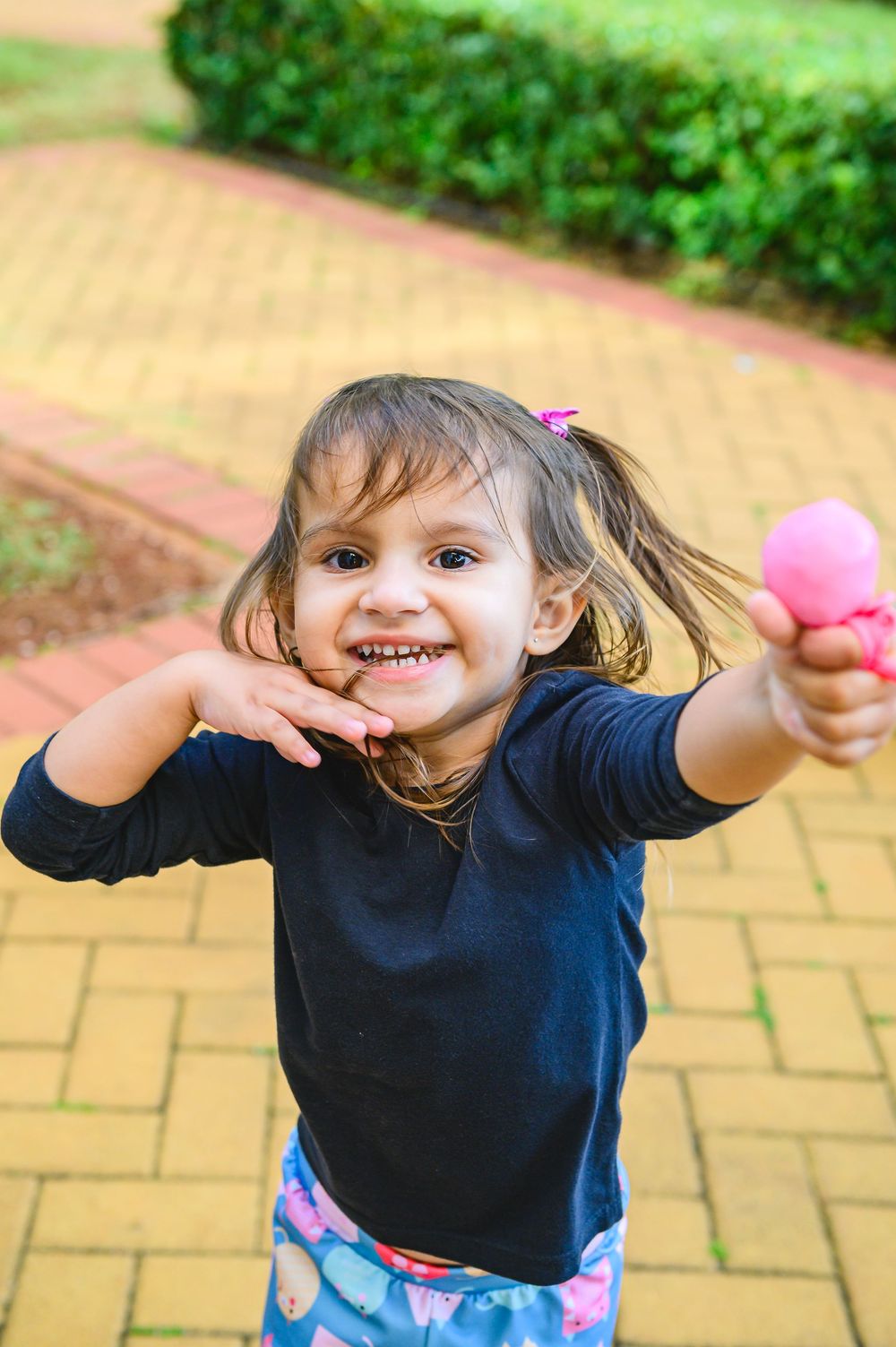 A child in a navy blue shirt and floral pants playfully dances and moves across outdoor brick pavement.
