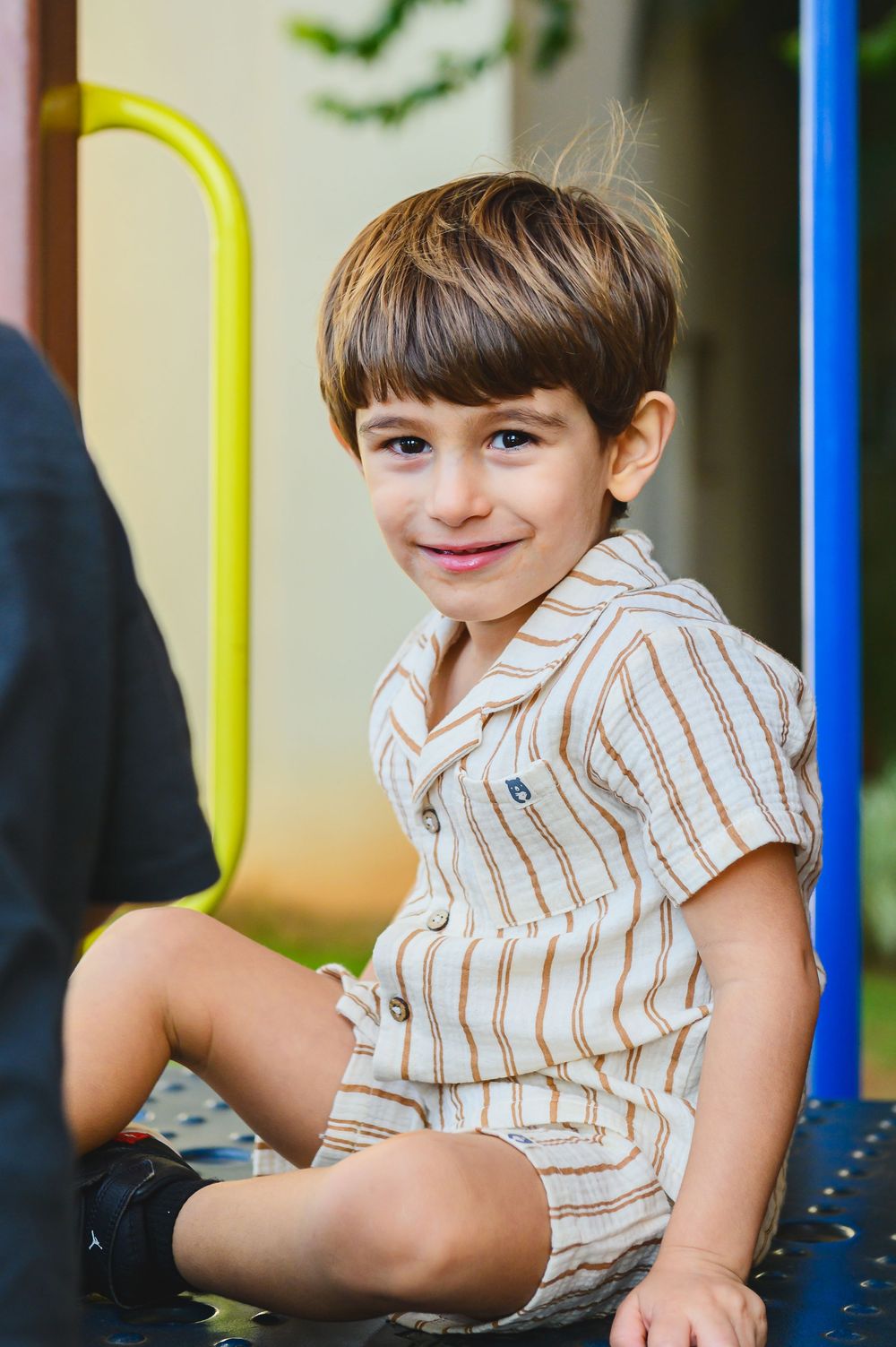 Young child wearing striped shirt plays and smiles while sitting at a playground structure.