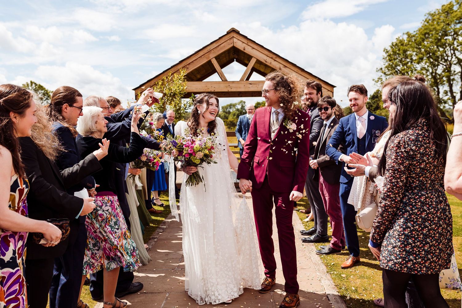 A romantic outdoor wedding scene with wildflowers, as a couple walks down a path together under an umbrella in nature.