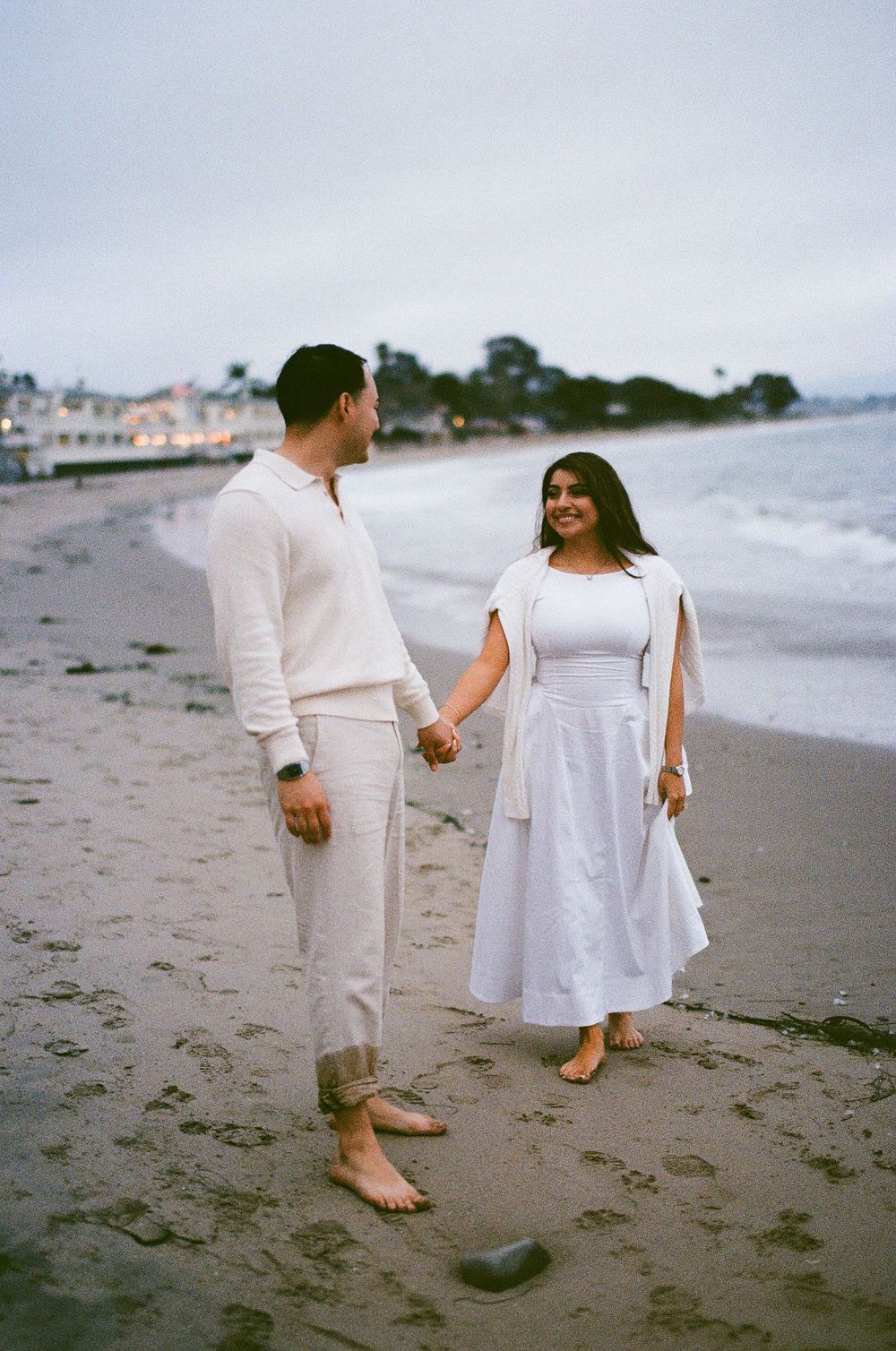 Couple walking barefoot along the shoreline after beach proposal.