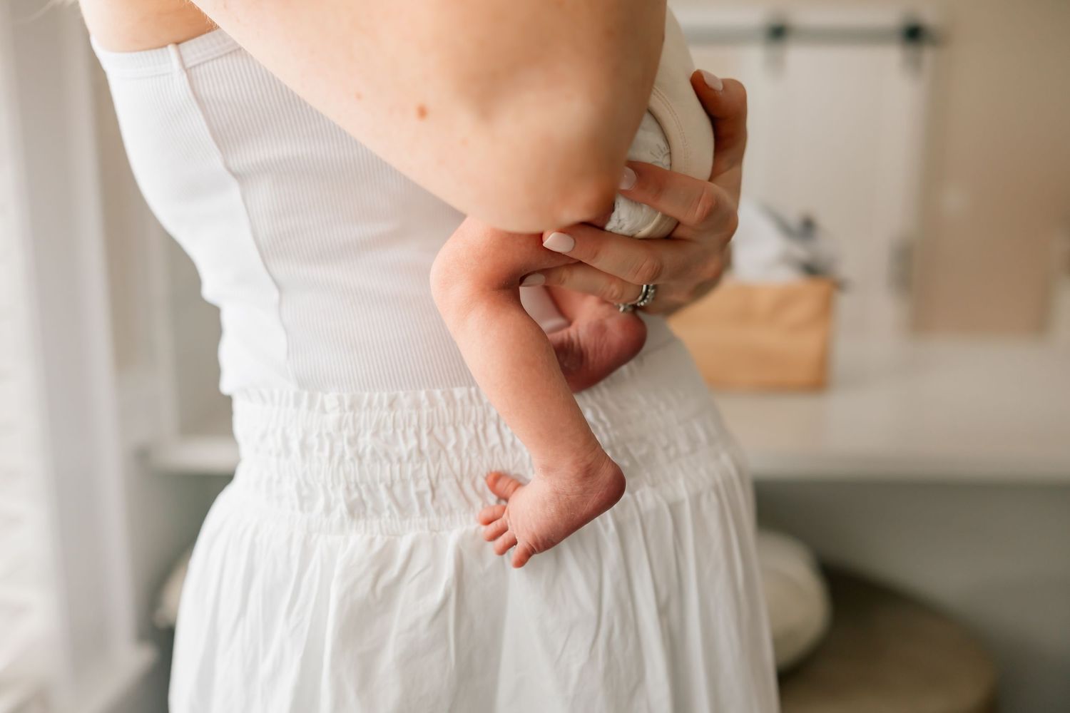 A tiny baby foot is held against a white dress with smocked waistline detail.