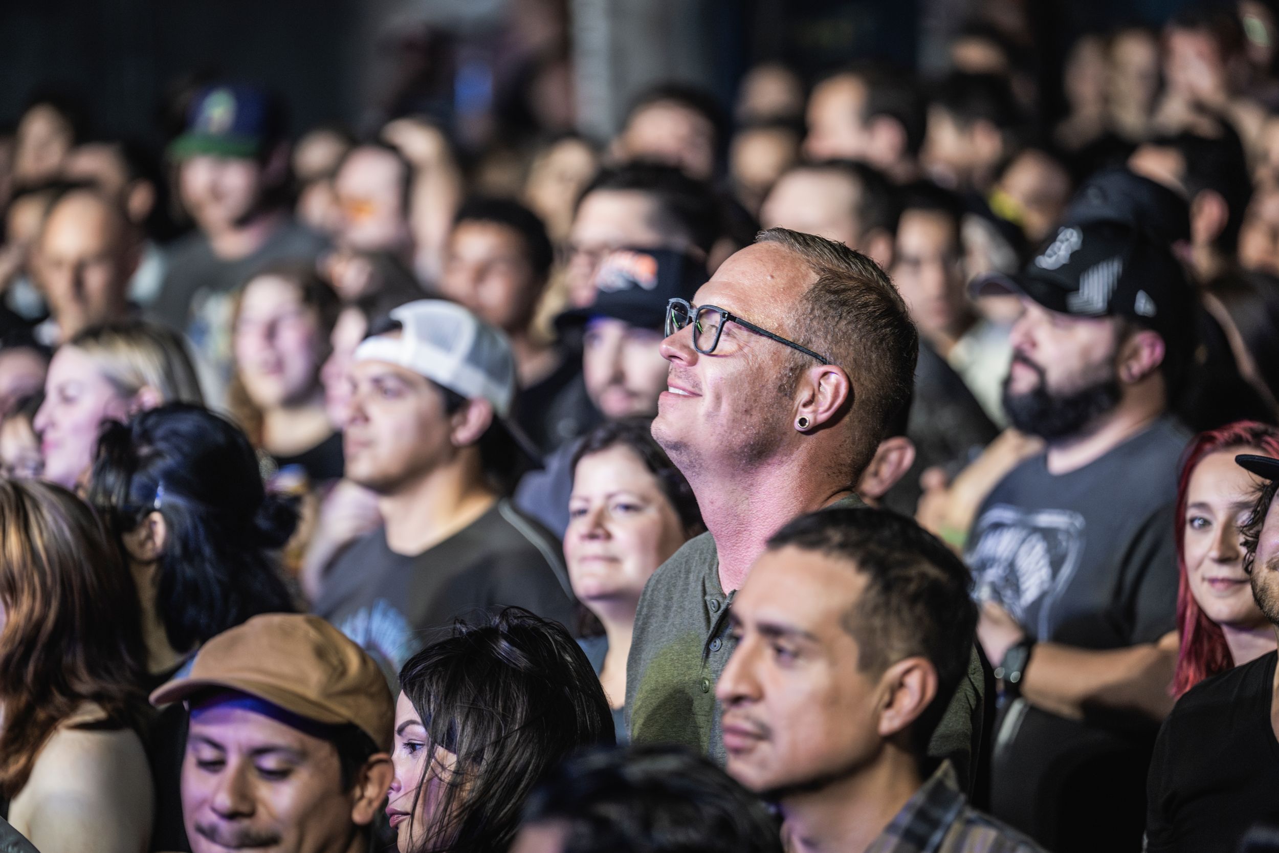 A crowd of focused concert-goers watches intently during a live performance in a dimly lit venue.