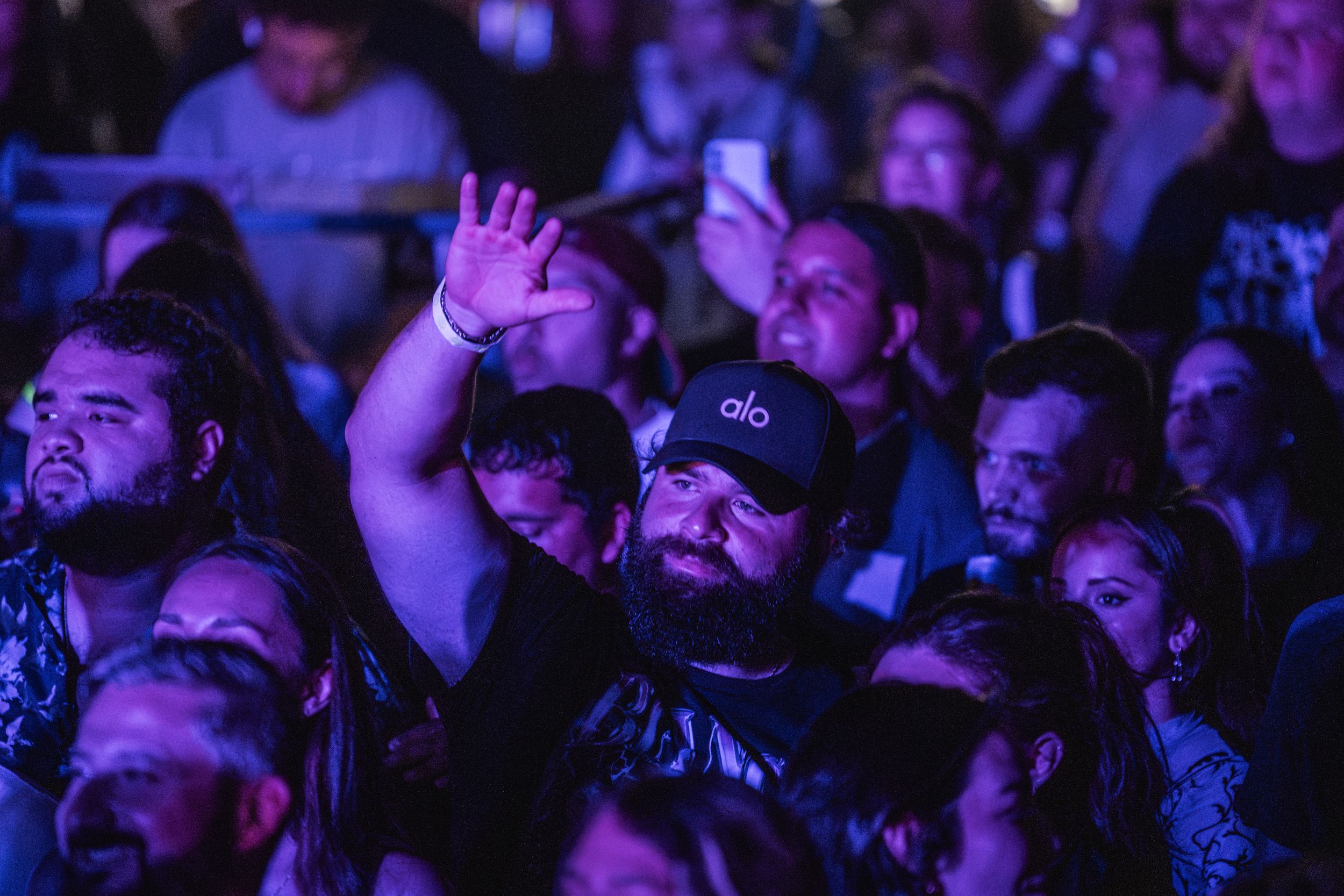 Concert crowd watching a performance illuminated by purple lighting in a dark venue.