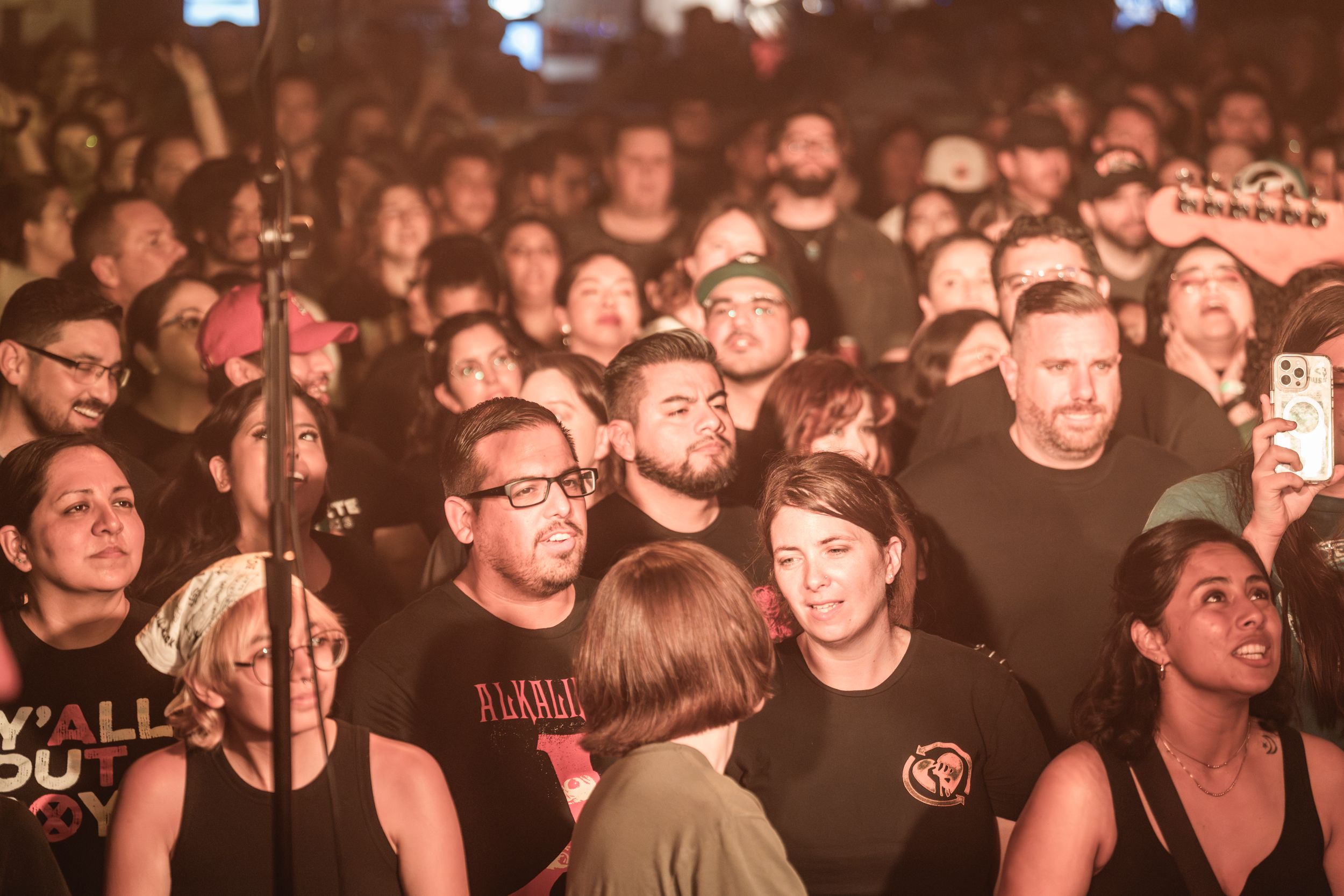 A crowded music concert audience watches a performance with warm lighting illuminating the passionate crowd.