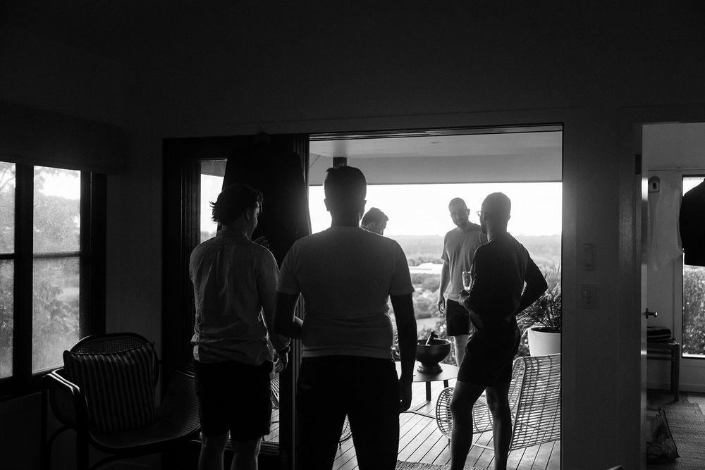 Silhouettes of people stand against a bright window creating dramatic contrast in black and white photography.