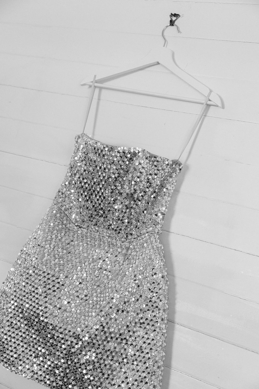 A sparkly silver sequined cocktail dress with a strapless design hangs on a white hanger against a light background.