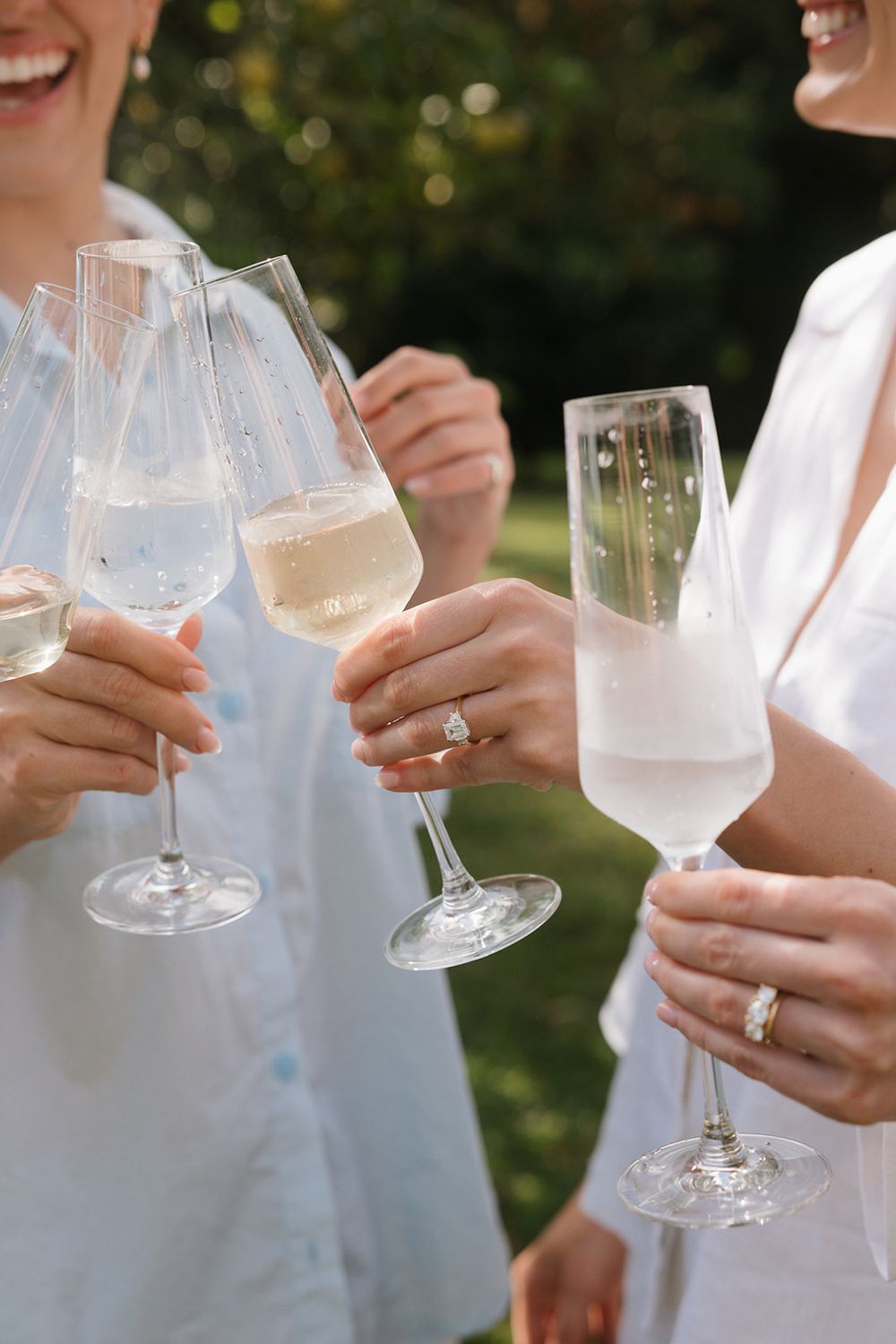 Close-up view of people toasting with white wine glasses outdoors on a sunny day.