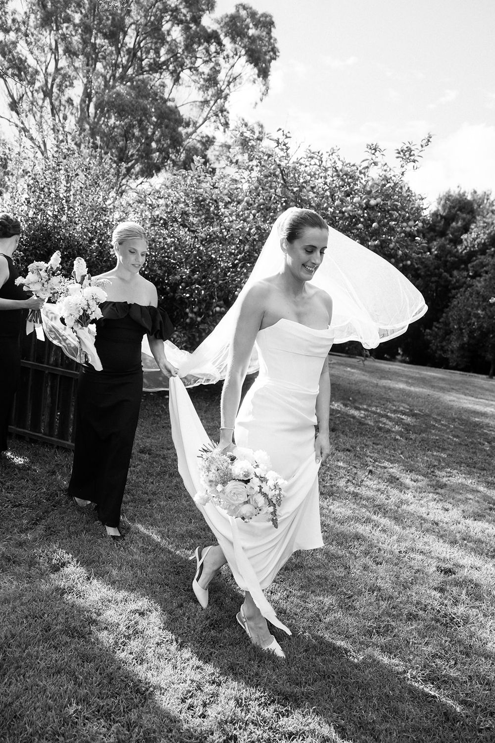 A black and white photo of a wedding dress flowing in the breeze on a grassy lawn.