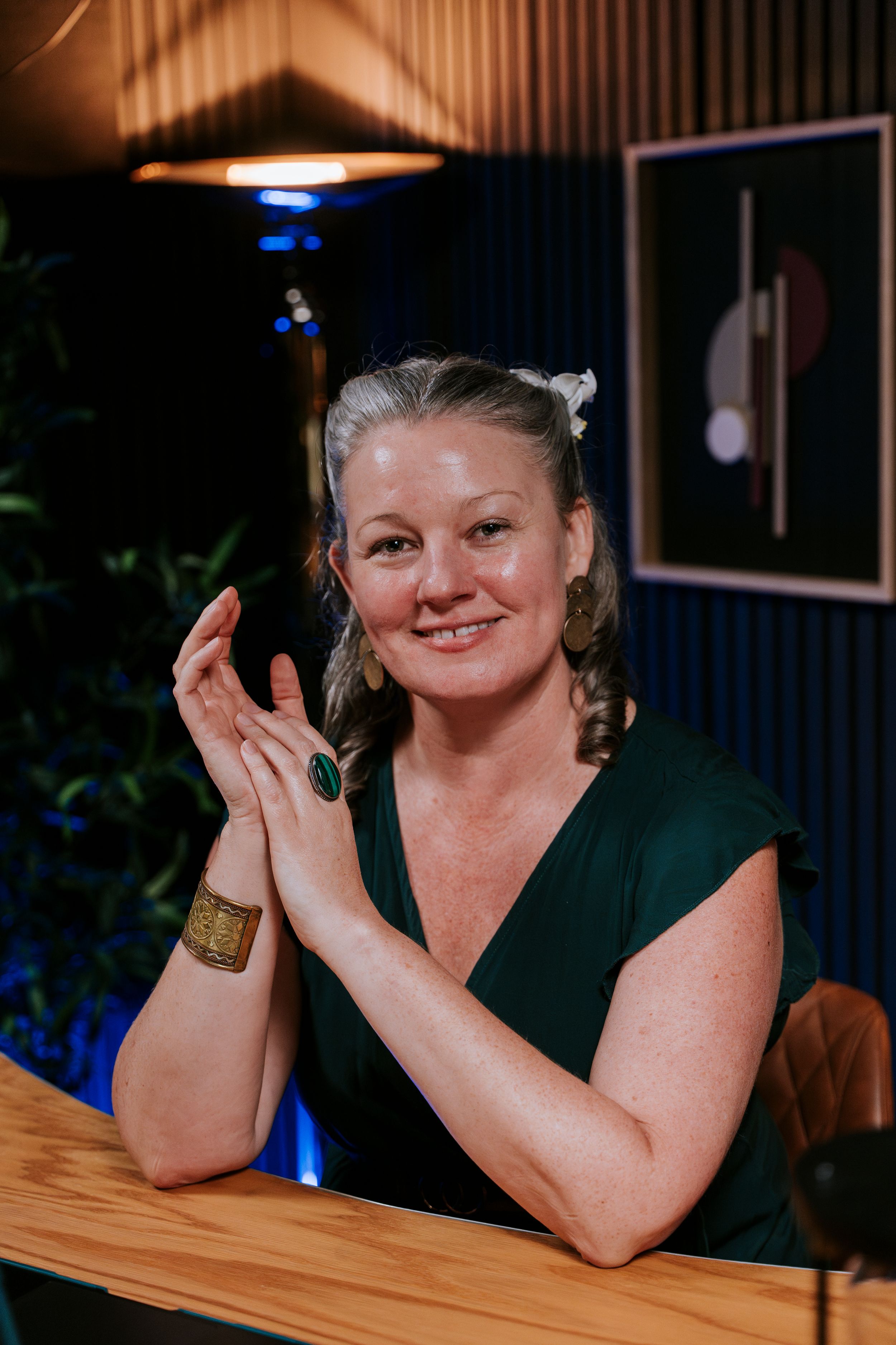 A woman in a black top leans on a wooden table while smiling and posing expressively in a sequence of photos.