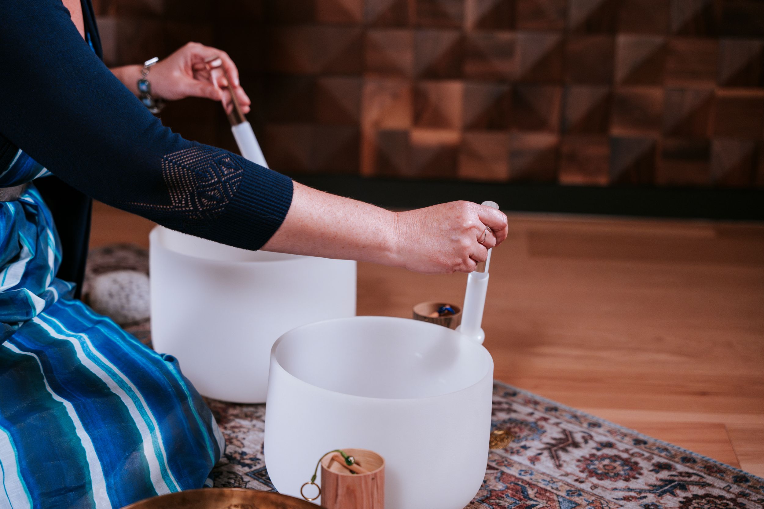 Someone practices sound healing with white quartz crystal singing bowls on a patterned rug.
