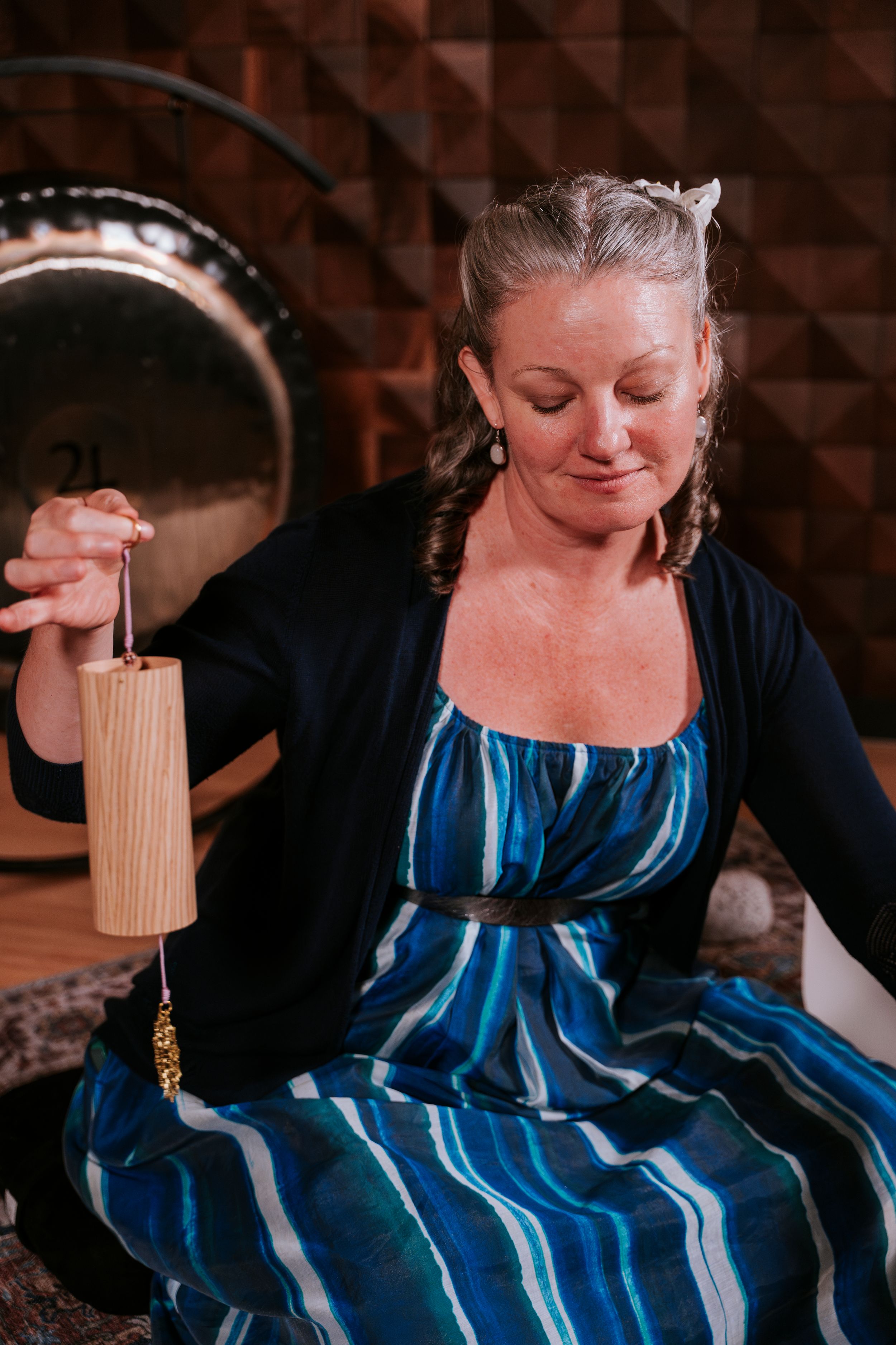 Woman in blue striped dress demonstrates traditional hand spinning technique with natural fiber.