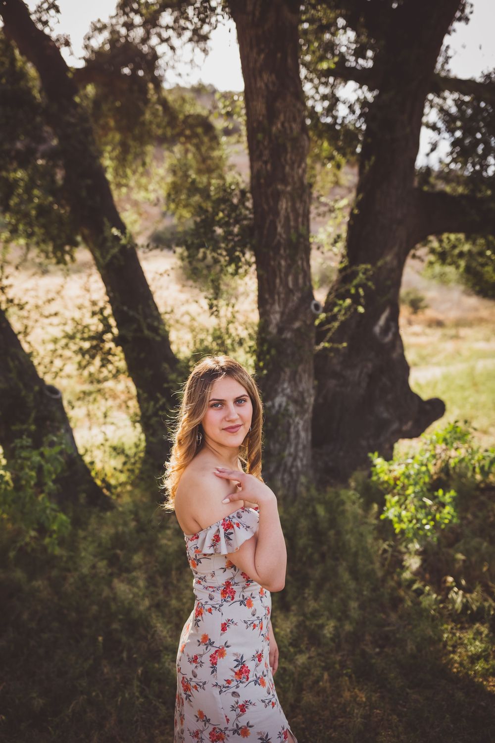 Ethereal outdoor portrait in a floral dress among oak trees during golden hour.