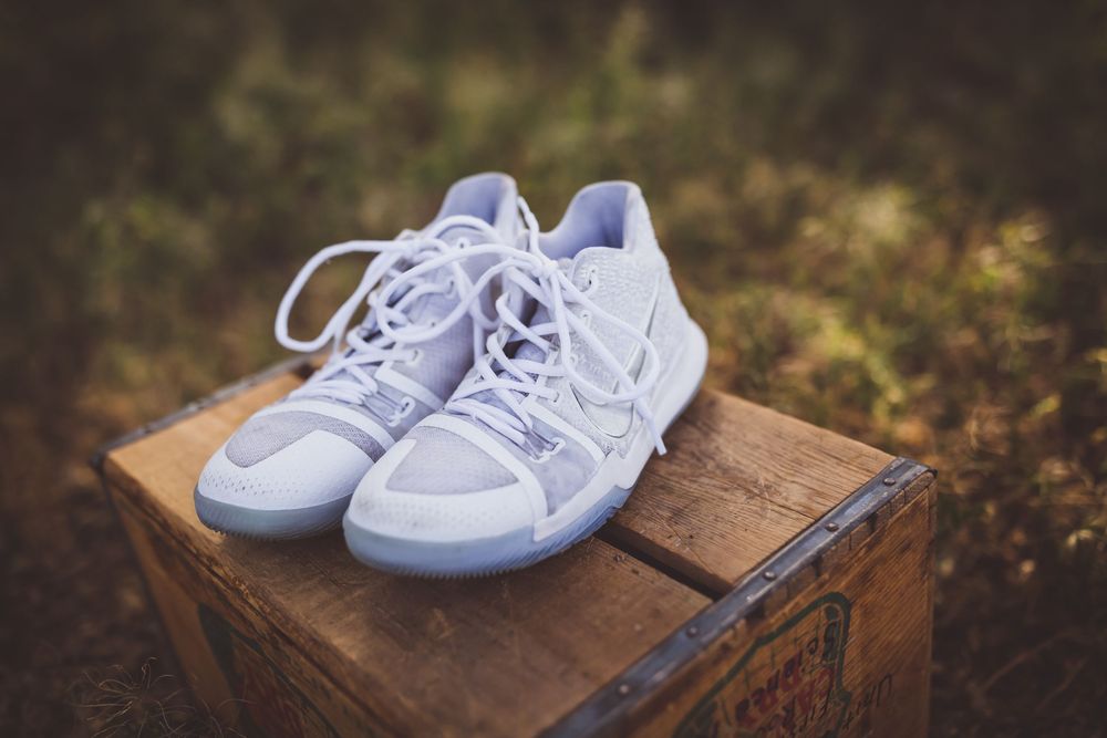 A pair of white sneakers placed on a rustic wooden surface in an outdoor garden setting.