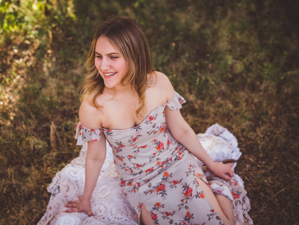 Woman in off-shoulder floral print dress poses elegantly in a natural outdoor setting among trees.