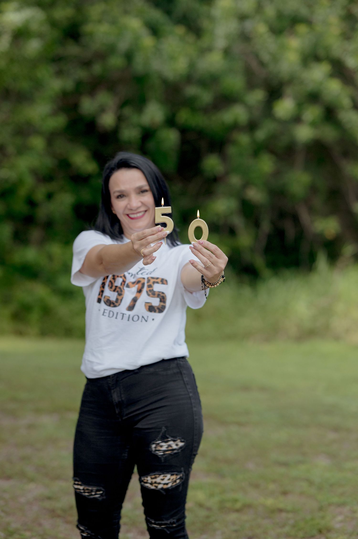 Someone holding up golden number candles against a blurred green outdoor background.