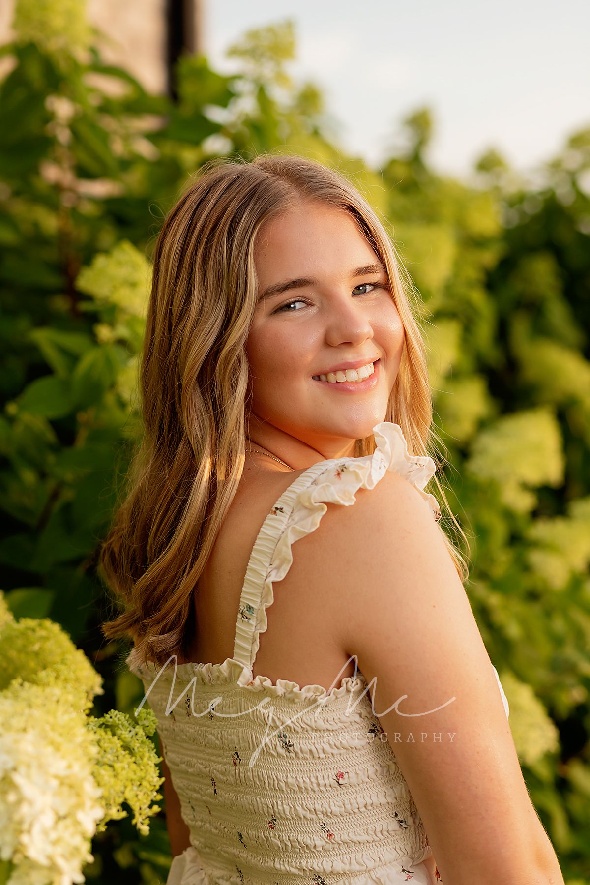 Teen girl in a ruffled cream dress outdoors with natural, sunlit background of greenery. Senior Pictures with MegMc Photography, Medina, TN