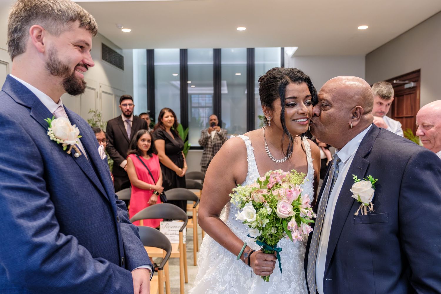 A joyful moment at a bright indoor wedding ceremony with floral bouquets and formal attire.