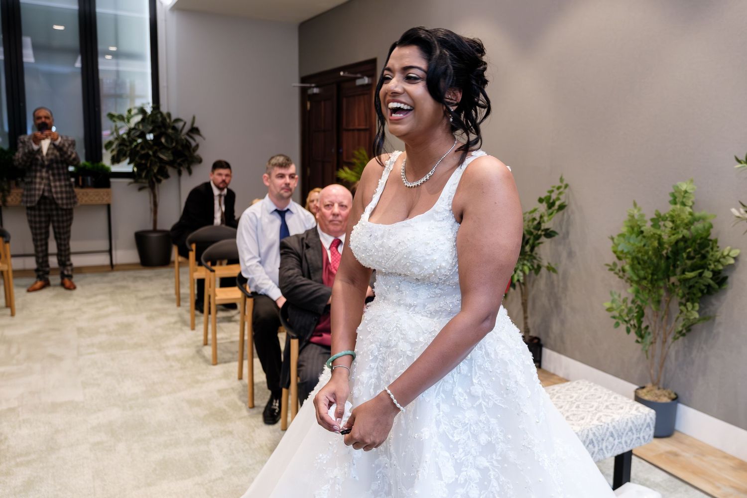 A group of people celebrate at a formal event with white floral decorations and light-colored walls.