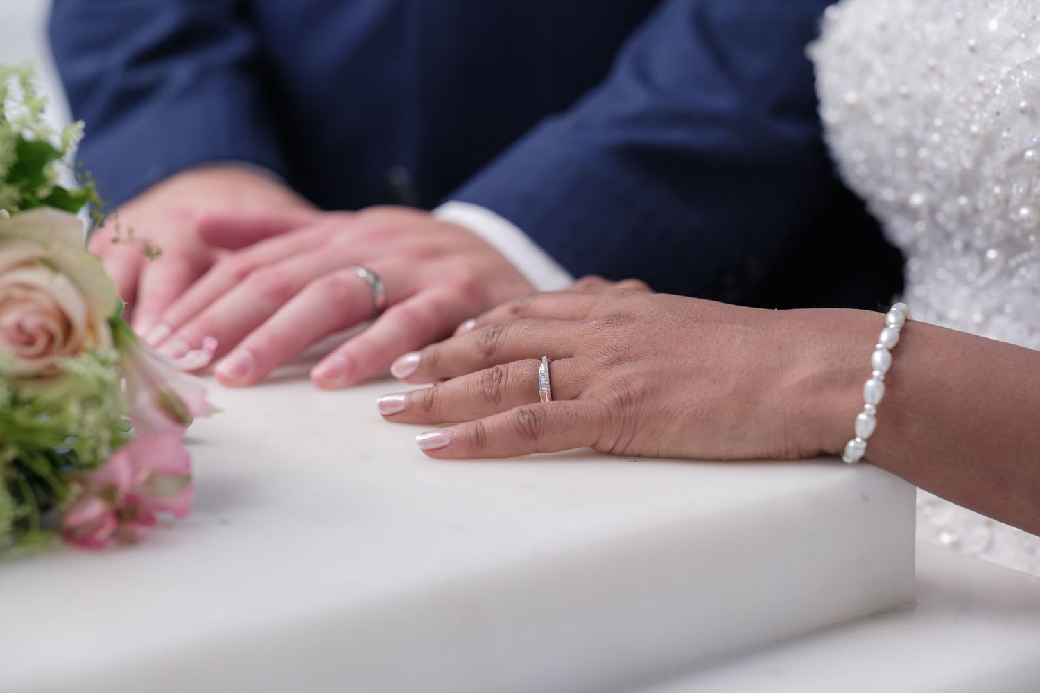 Wedding detail photo featuring hands of a newlywed couple, resting together with rings and elegant sleeve detail.