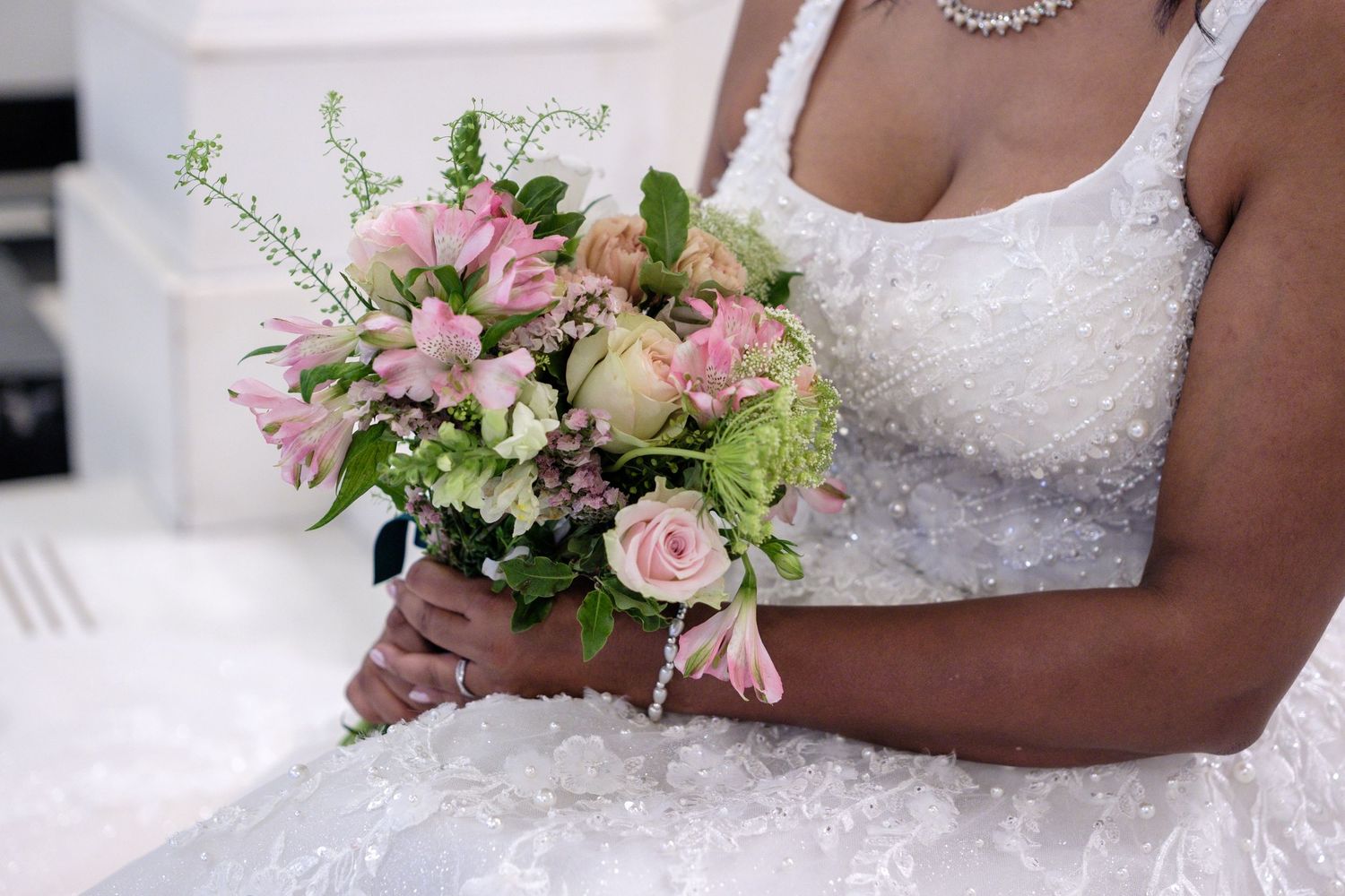 A delicate bridal bouquet of pink roses and greenery rests against a white lace wedding dress.