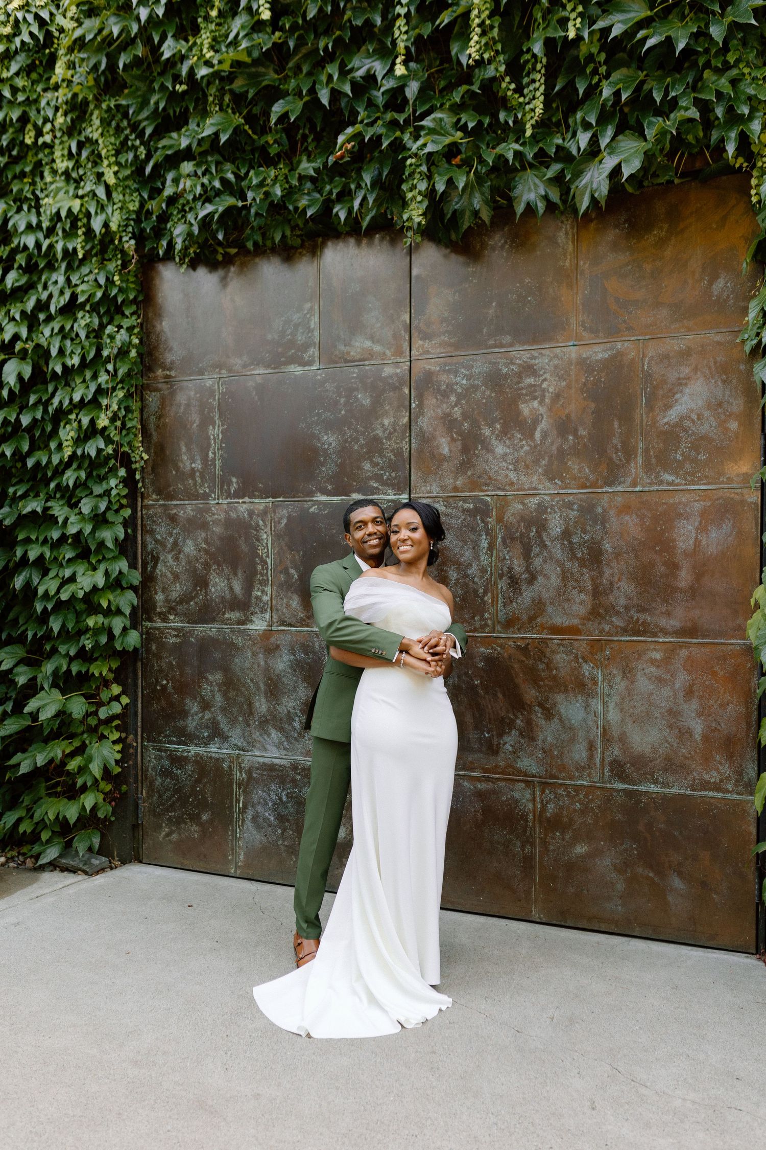 A couple shares a romantic moment against an ivy-covered wall with a metallic door background.