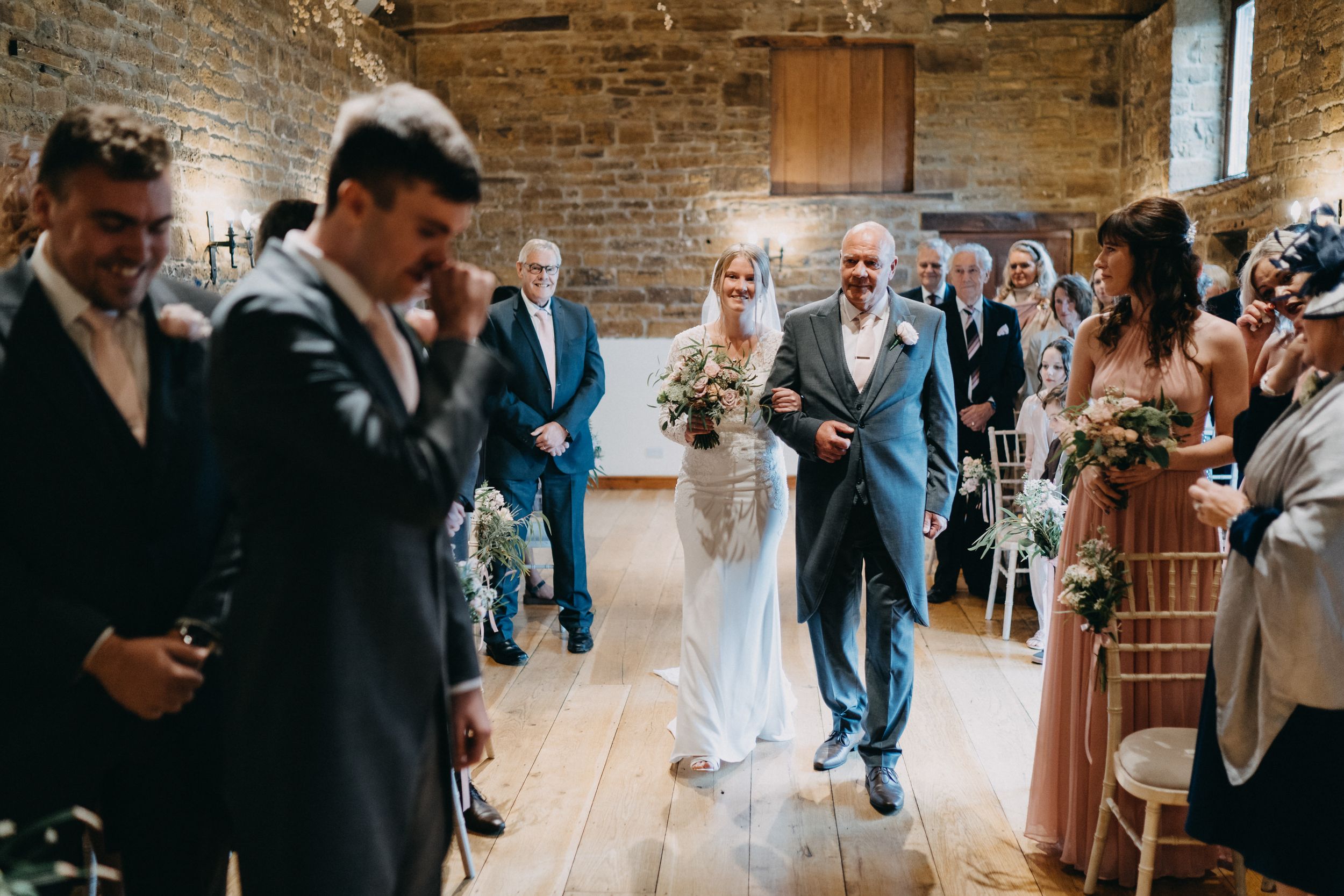 Wedding processional in rustic brick venue with guests seated along aisle.