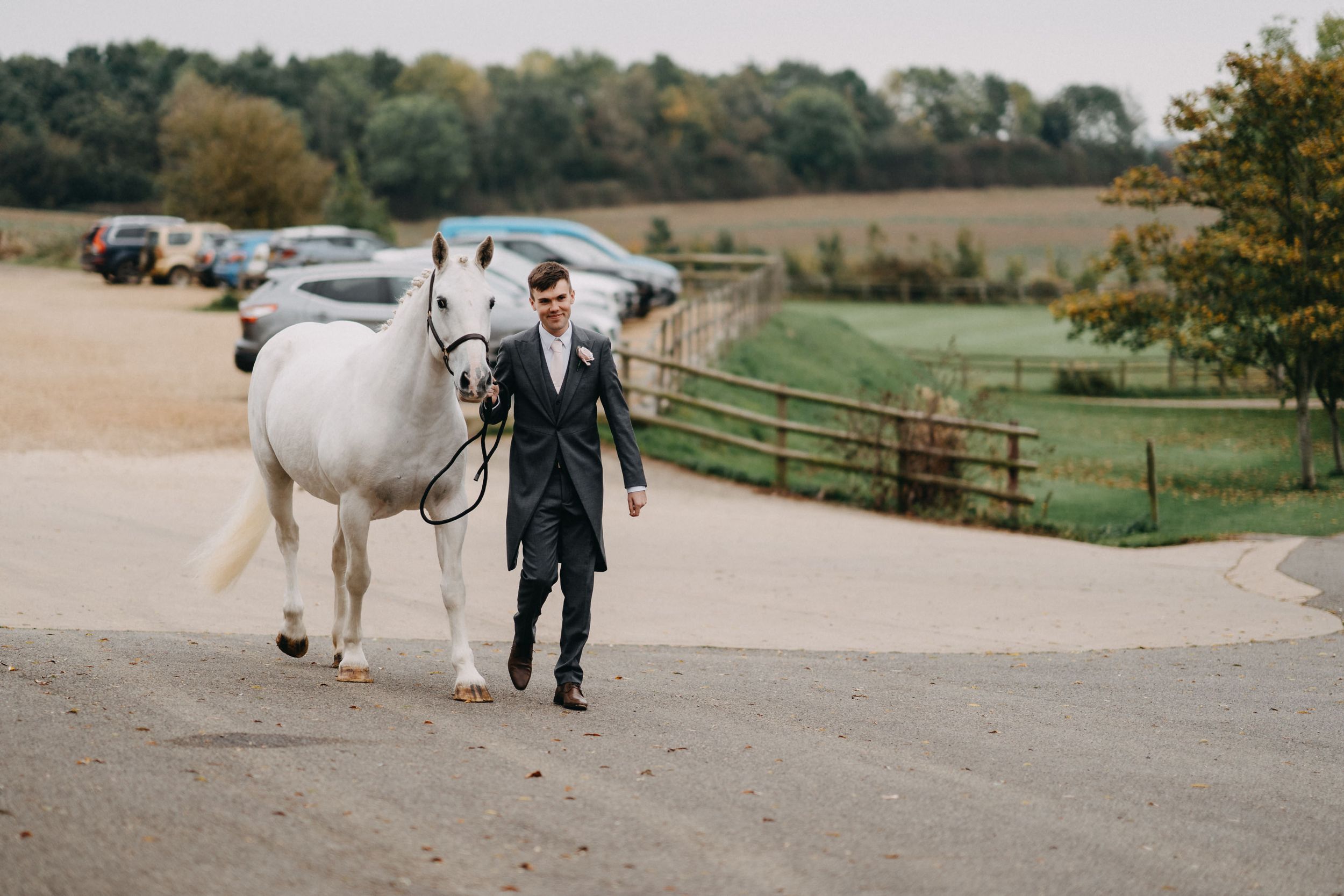 The Groom walking with beautiful white horse along countryside path at Crockwell Farm, Northamptonshire.