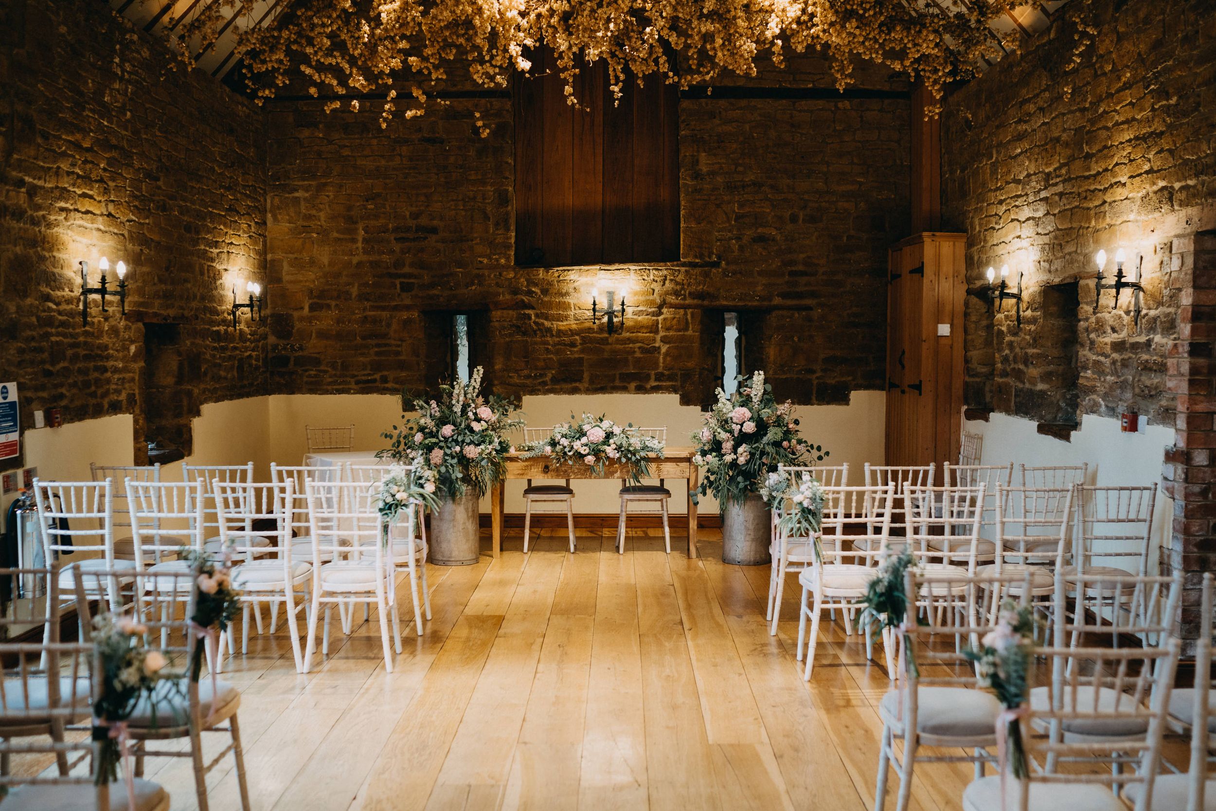 Elegant wedding ceremony setup at Crockwell Farm with white chairs and floral arrangements in a rustic brick-walled venue.