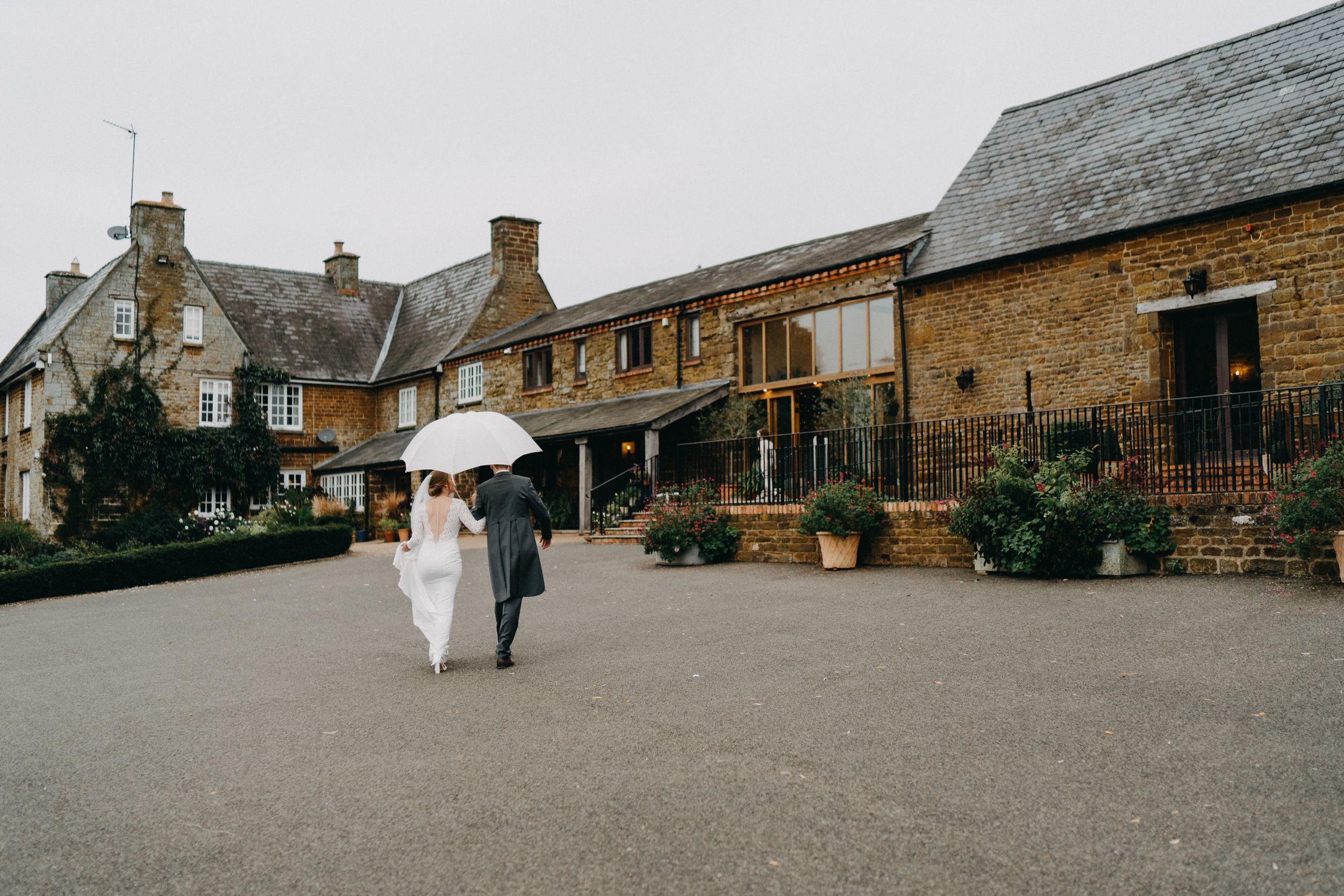 Wedding couple walks under umbrella at rustic Crockwell Farm in countryside setting.