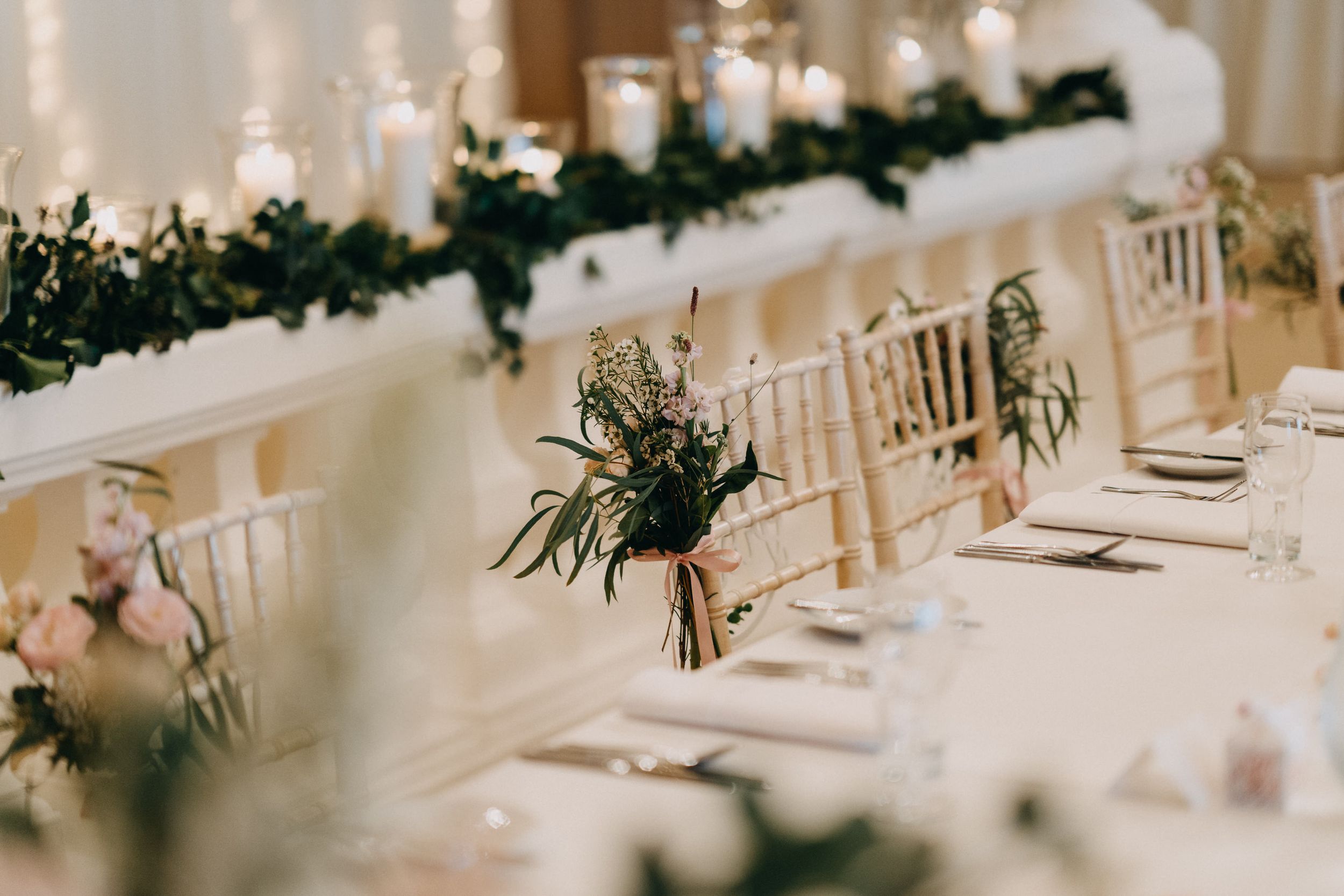 Elegant wedding table setting with white candles and greenery garland decorations.