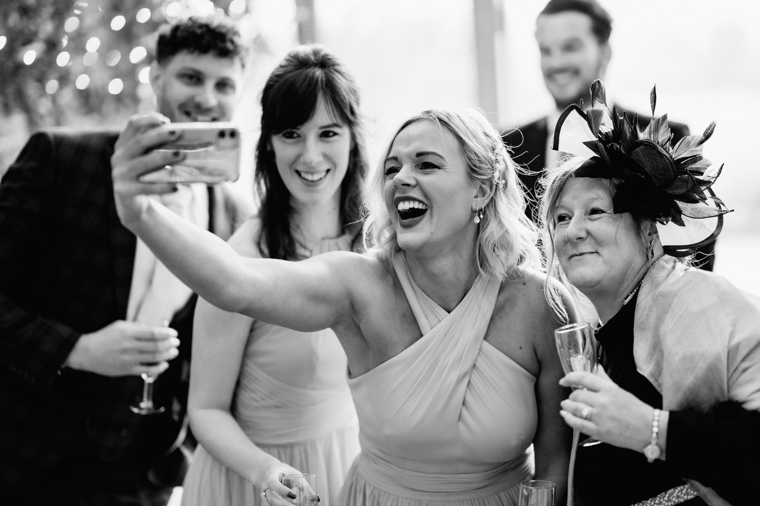 Wedding party members taking celebratory selfies with champagne glasses at reception.