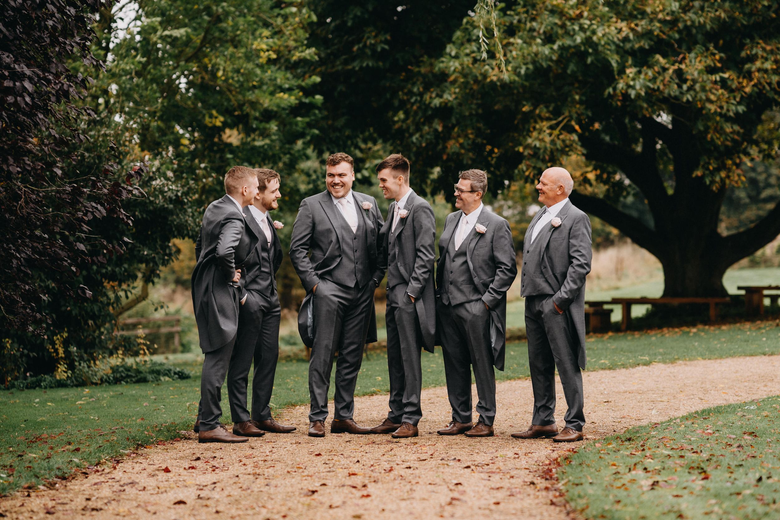 Wedding party in matching grey suits standing together on a garden path.