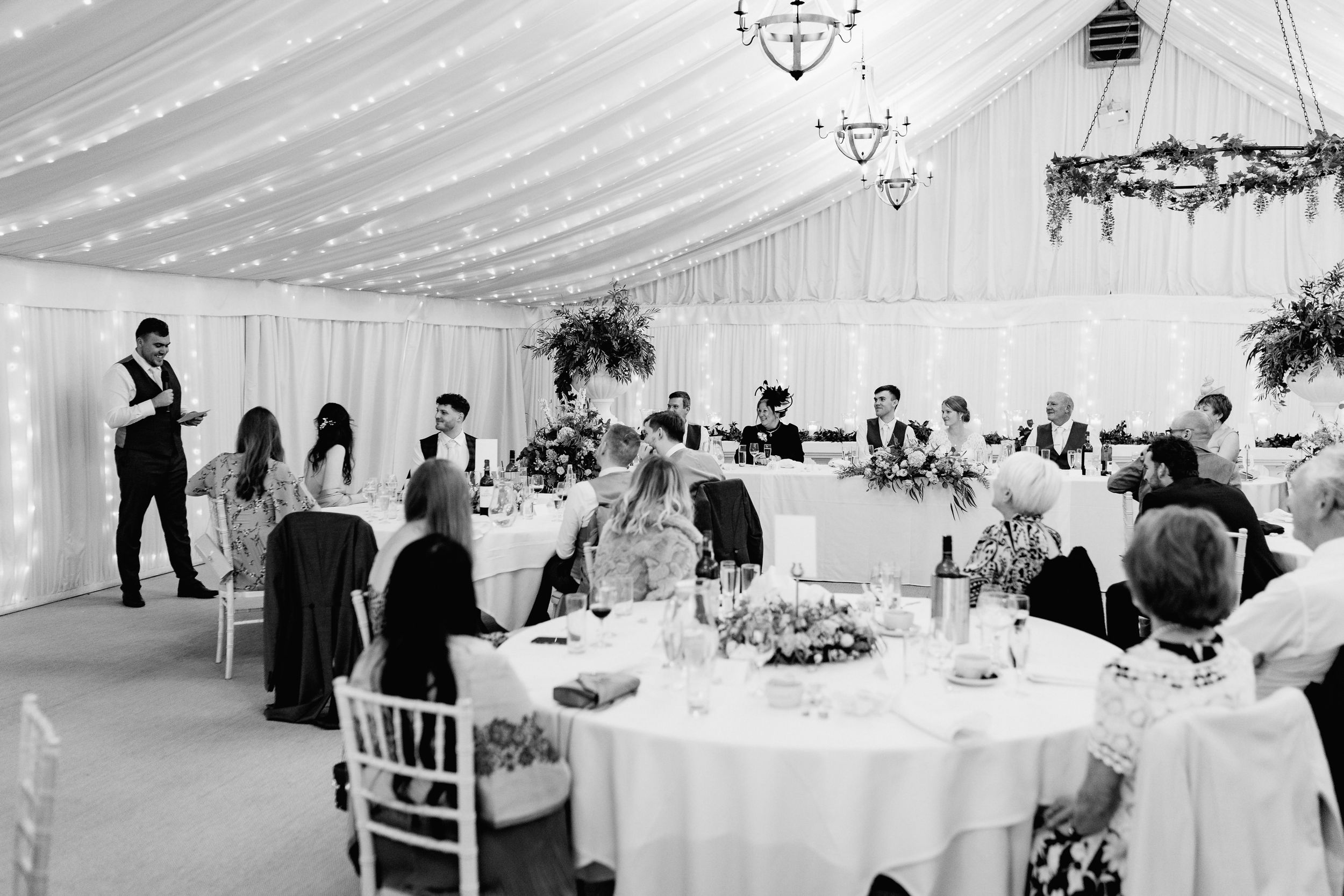 Wedding reception in an elegant white tent at Crockwell Farm with round tables and guests listening to a speaker.