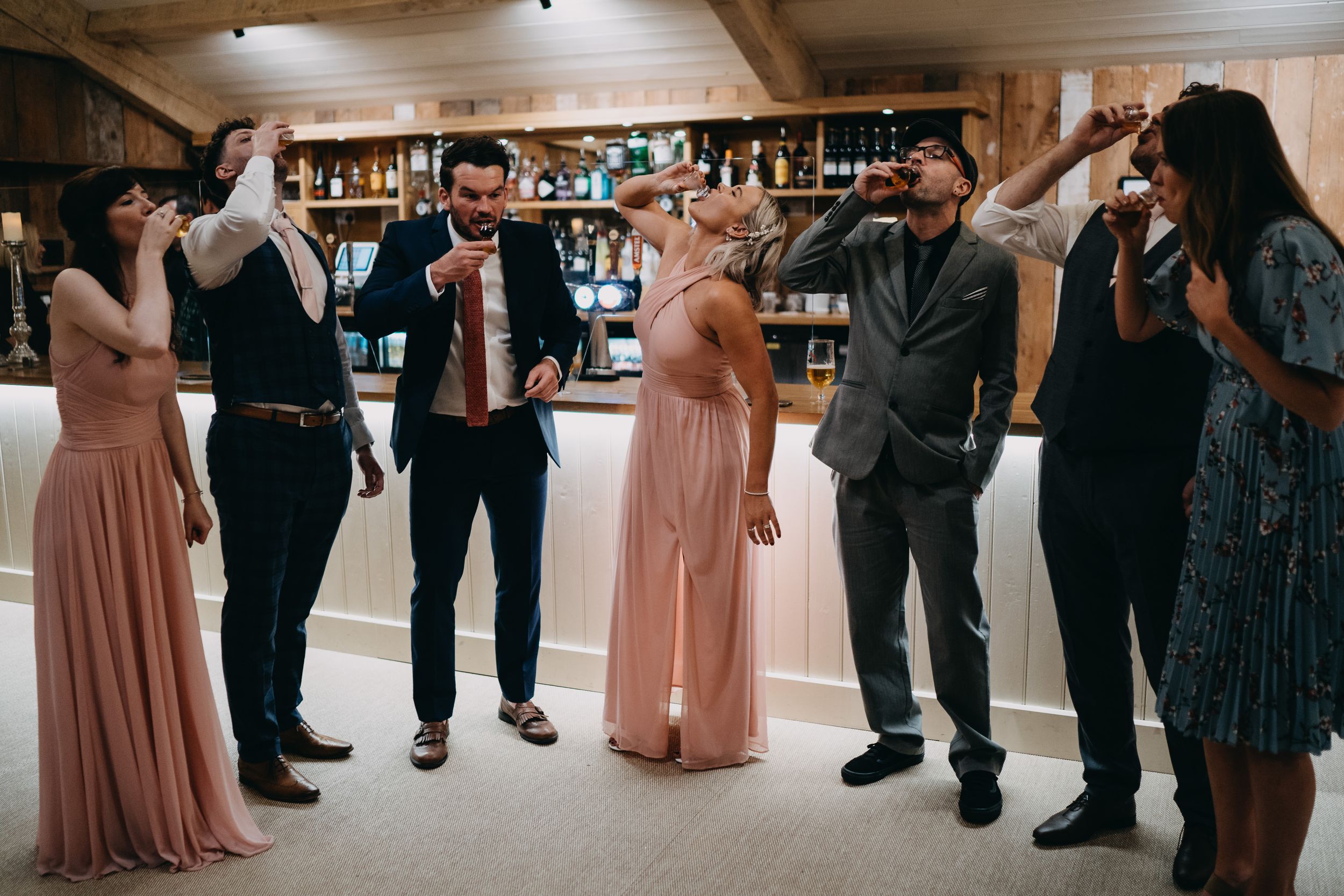 Wedding guests in formal attire singing and celebrating at a bar reception.