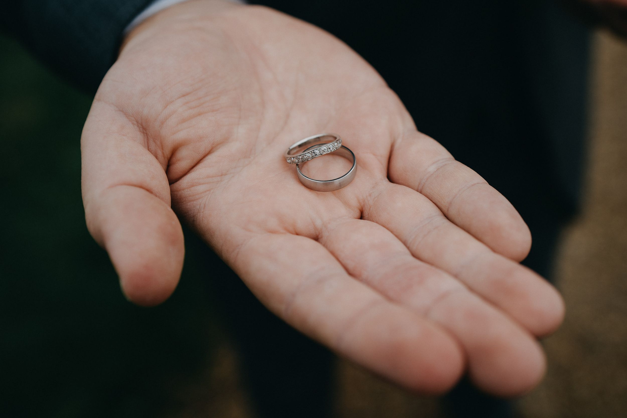 Wedding rings held in an open palm against a dark background.