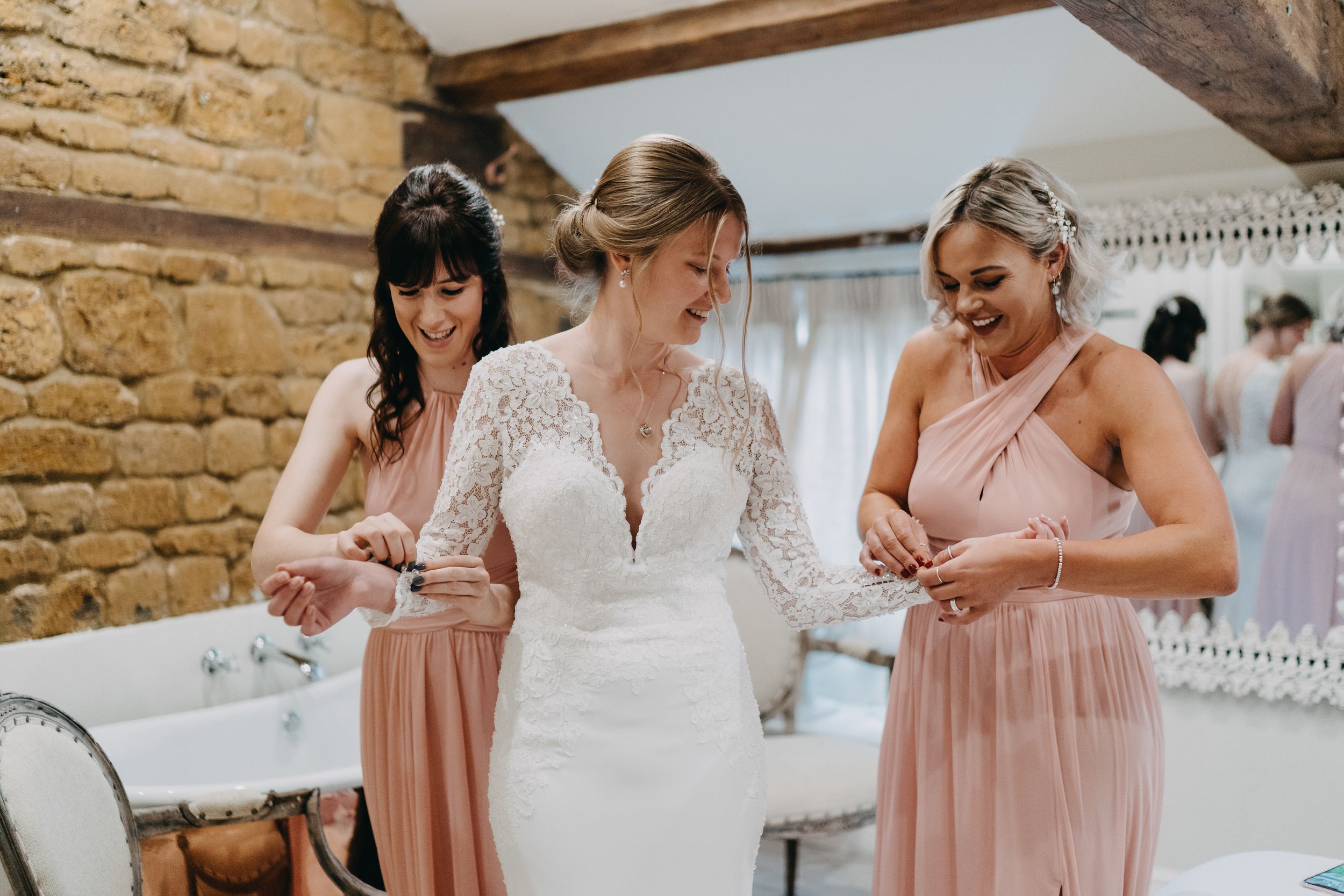 Wedding preparation scene with pink bridesmaid dresses in a stone-walled room.
