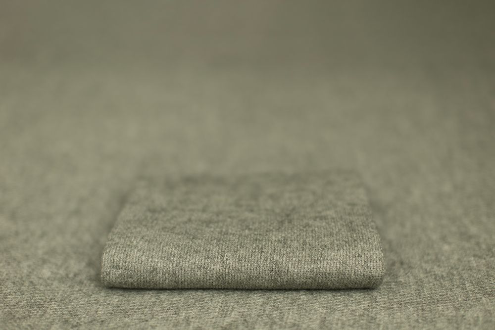 A folded gray linen or wool textile fabric sample sits on a neutral surface with shallow depth of field.