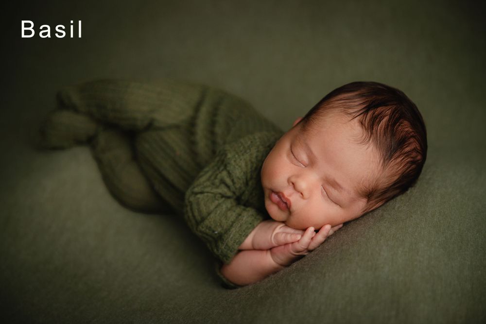Peaceful sleeping newborn baby wrapped in soft green fabric against matching green backdrop.