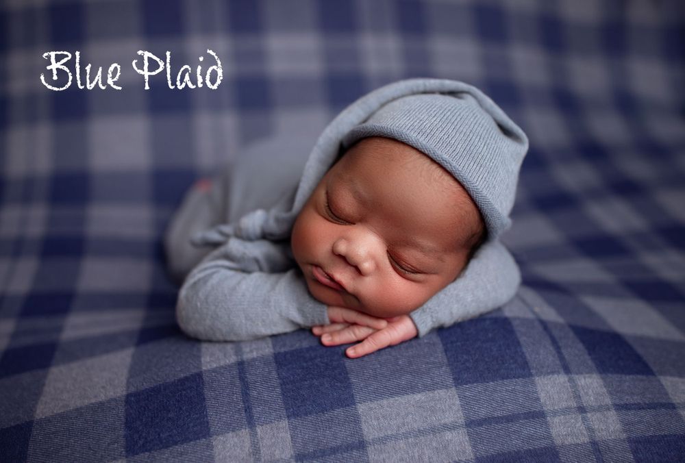 Sleeping newborn wearing soft gray outfit rests on blue plaid blanket during professional photo session.