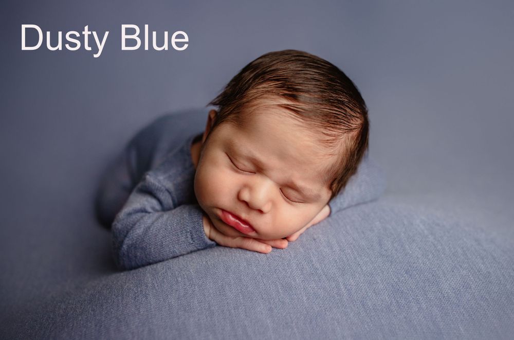 Sleeping newborn wearing dusty blue wrap rests peacefully on soft gray fabric background.