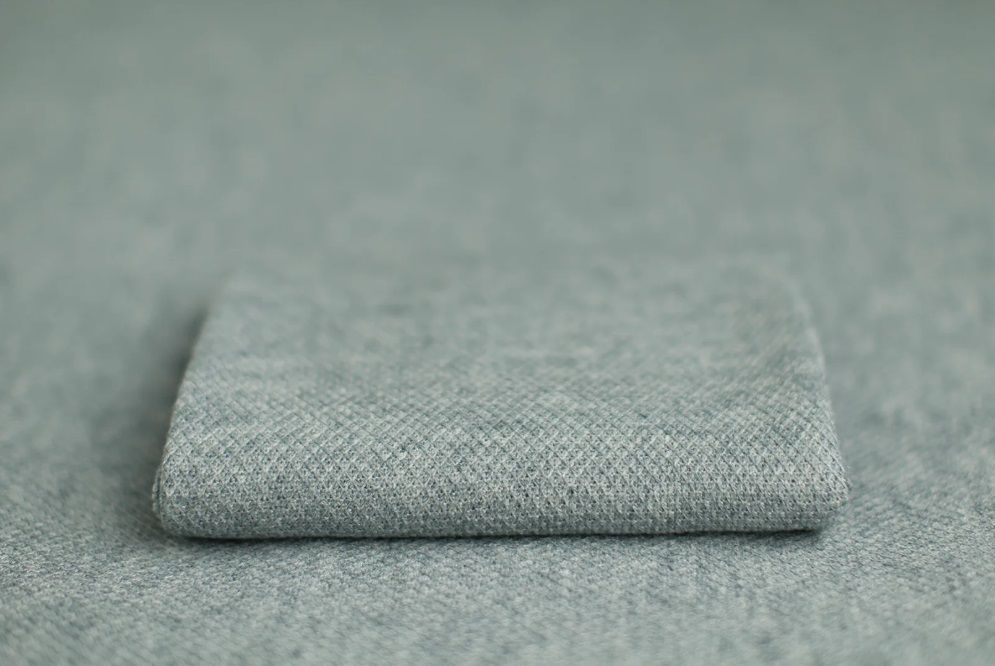 A neatly folded gray linen or wool fabric textile with visible texture against a soft gray background.