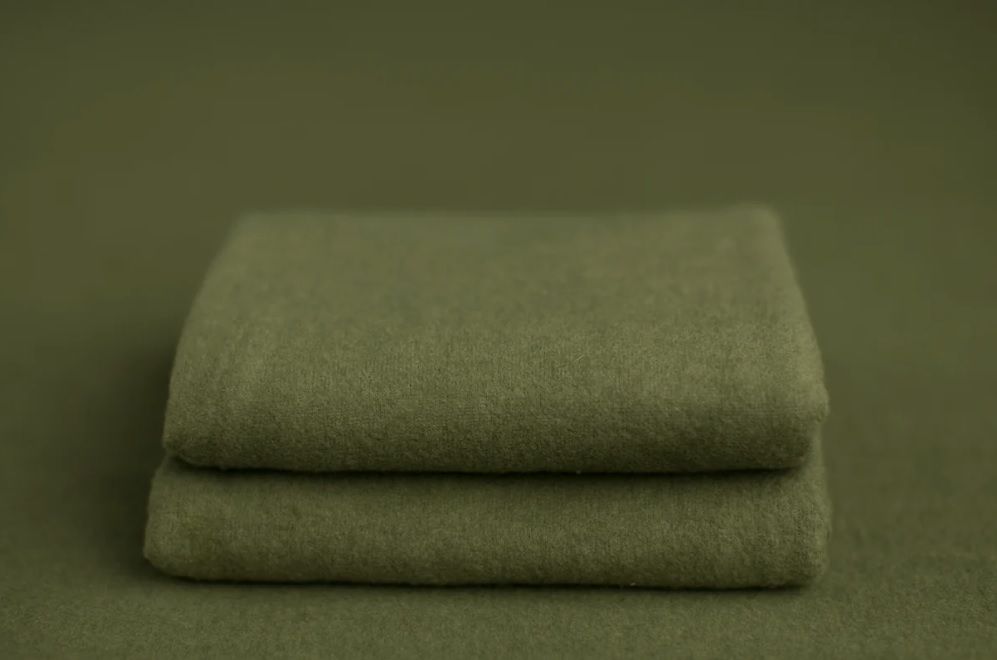 Two neatly folded sage green linen or cotton towels stacked on matching green background.
