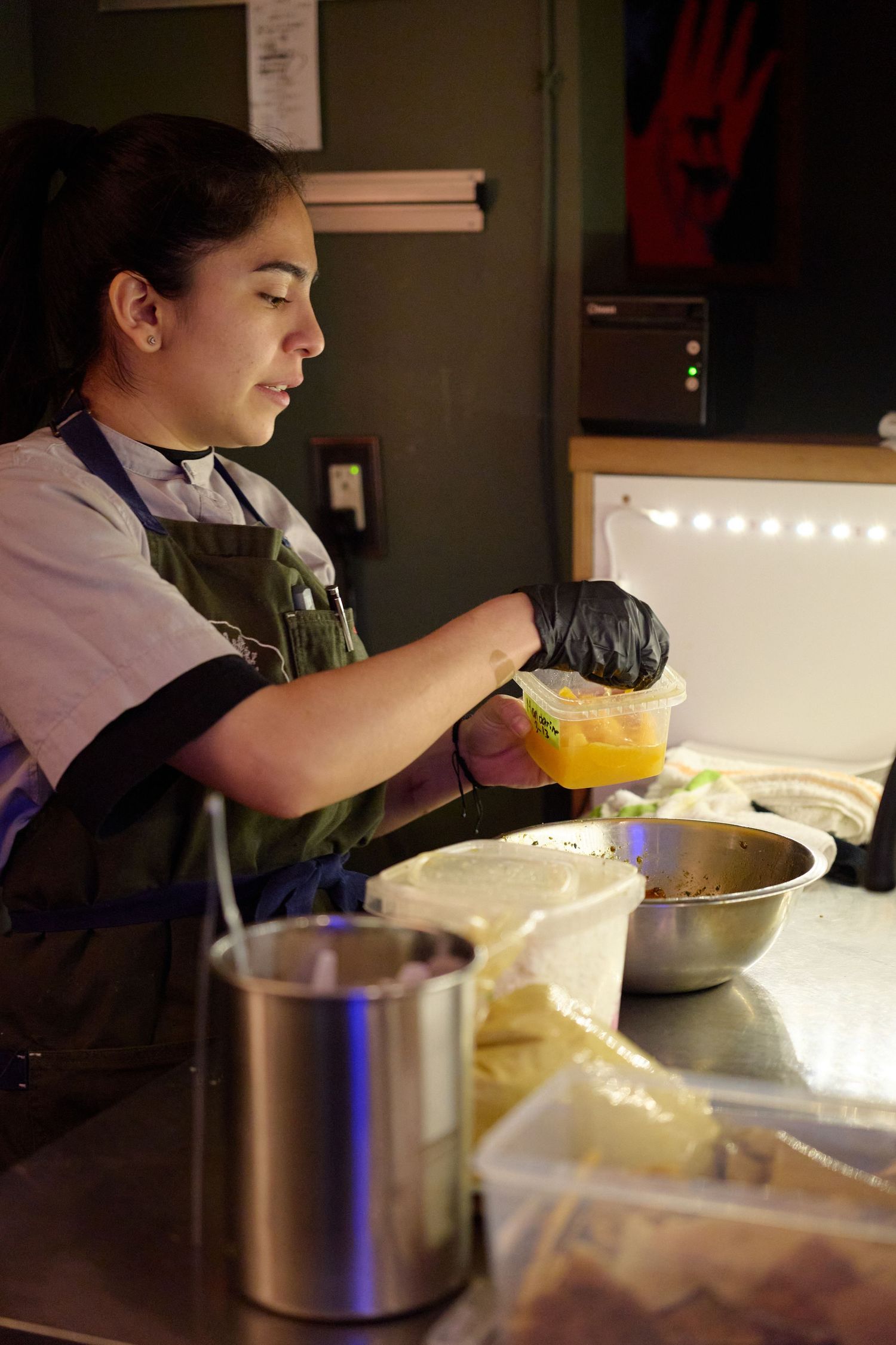 Restaurant worker in an apron preparing food ingredients at a prep station.