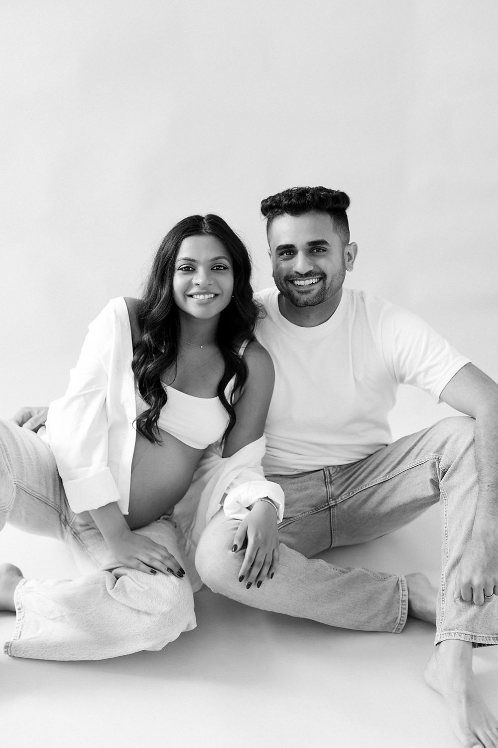 Black and white portrait of a couple sitting together on the floor wearing casual white outfits and denim.